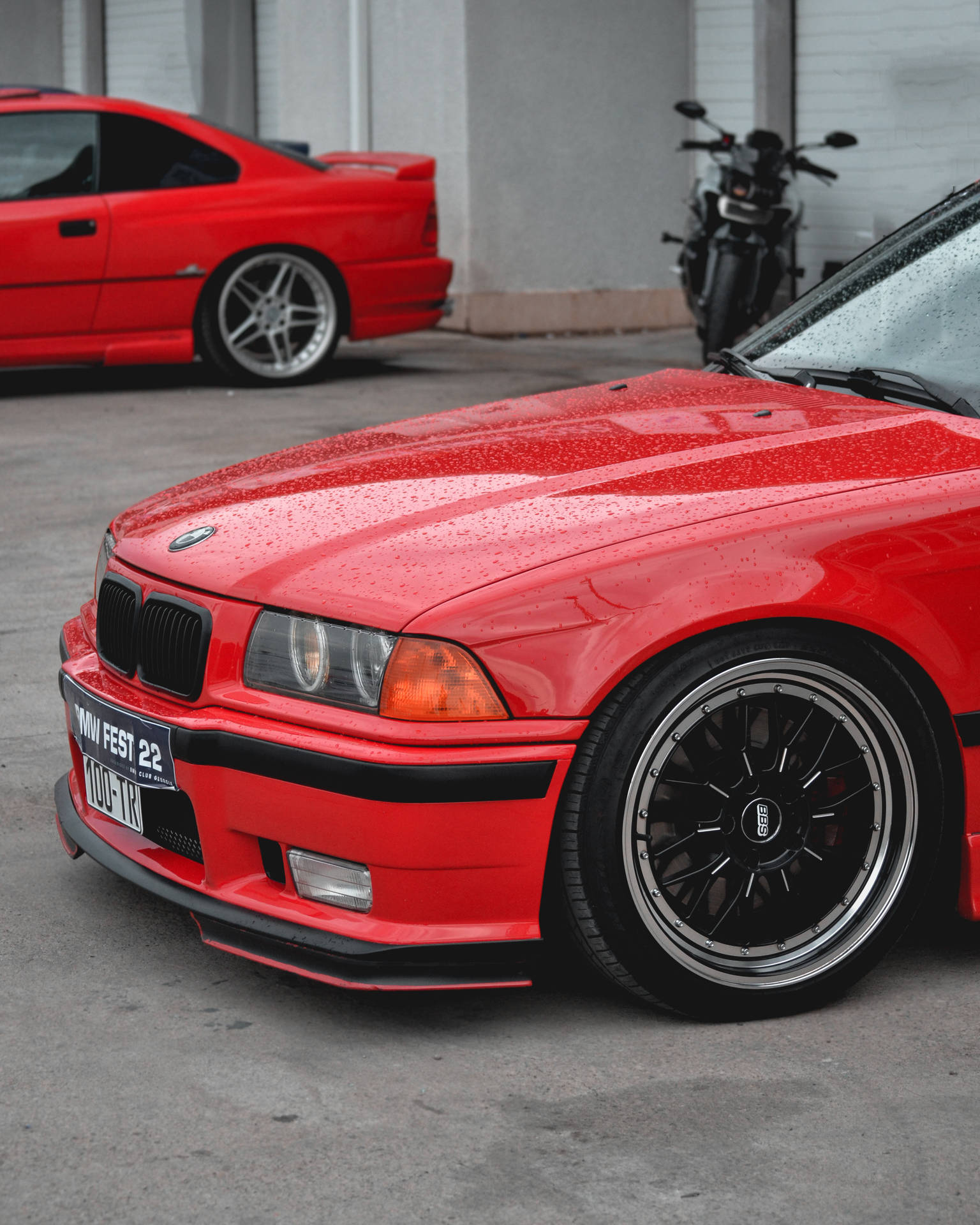 紅色BMW E36雙門轎跑車帶雨滴泊喺車庫入面電單車旁邊。