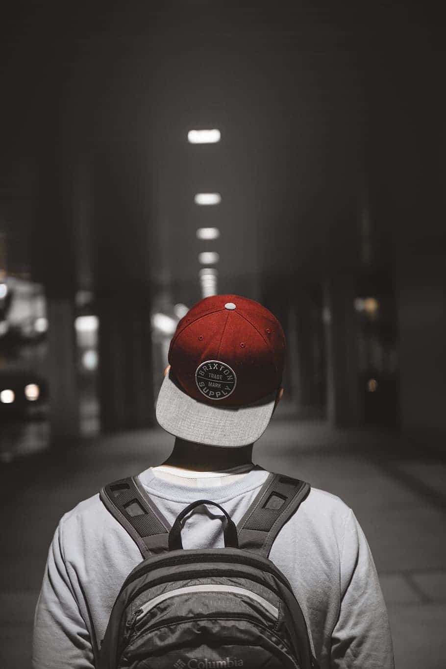 戴紅色帽子和背囊嘅人夜晚行喺黑暗嘅城市街道上。
