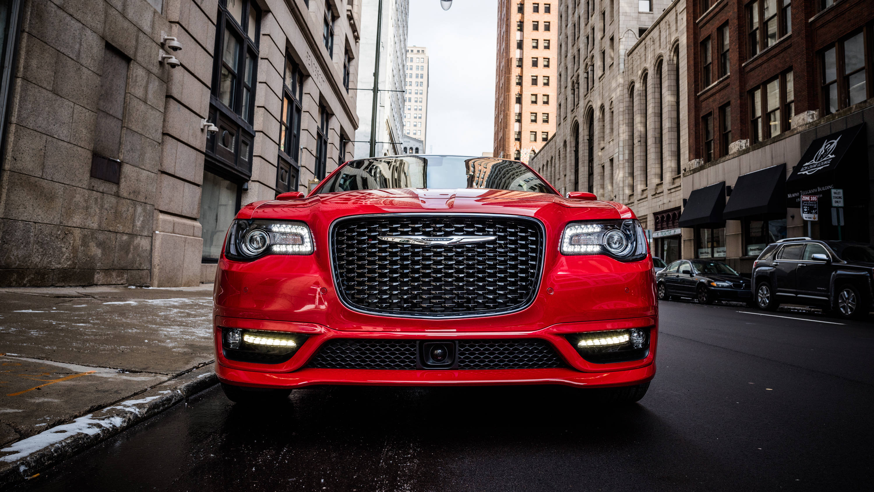 紅色 Chrysler 300 S 壁紙 — 一架亮紅色嘅Chrysler 300C開篷車停泊喺濕滑嘅城市街道上，兩旁係高聳嘅磚建築，天空多雲。