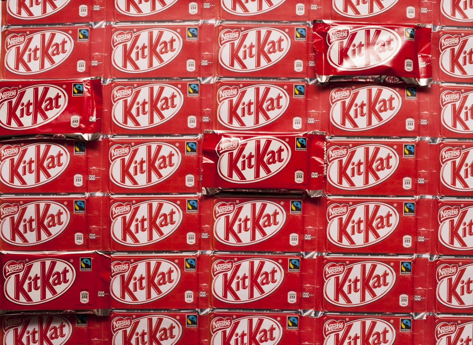 紅色 KitKat 巧克力 壁紙 — 密集的紅色KitKat朱古力棒包裝紙網格，以白色標誌和銀色箔片點綴，形成大膽的重複圖案。
