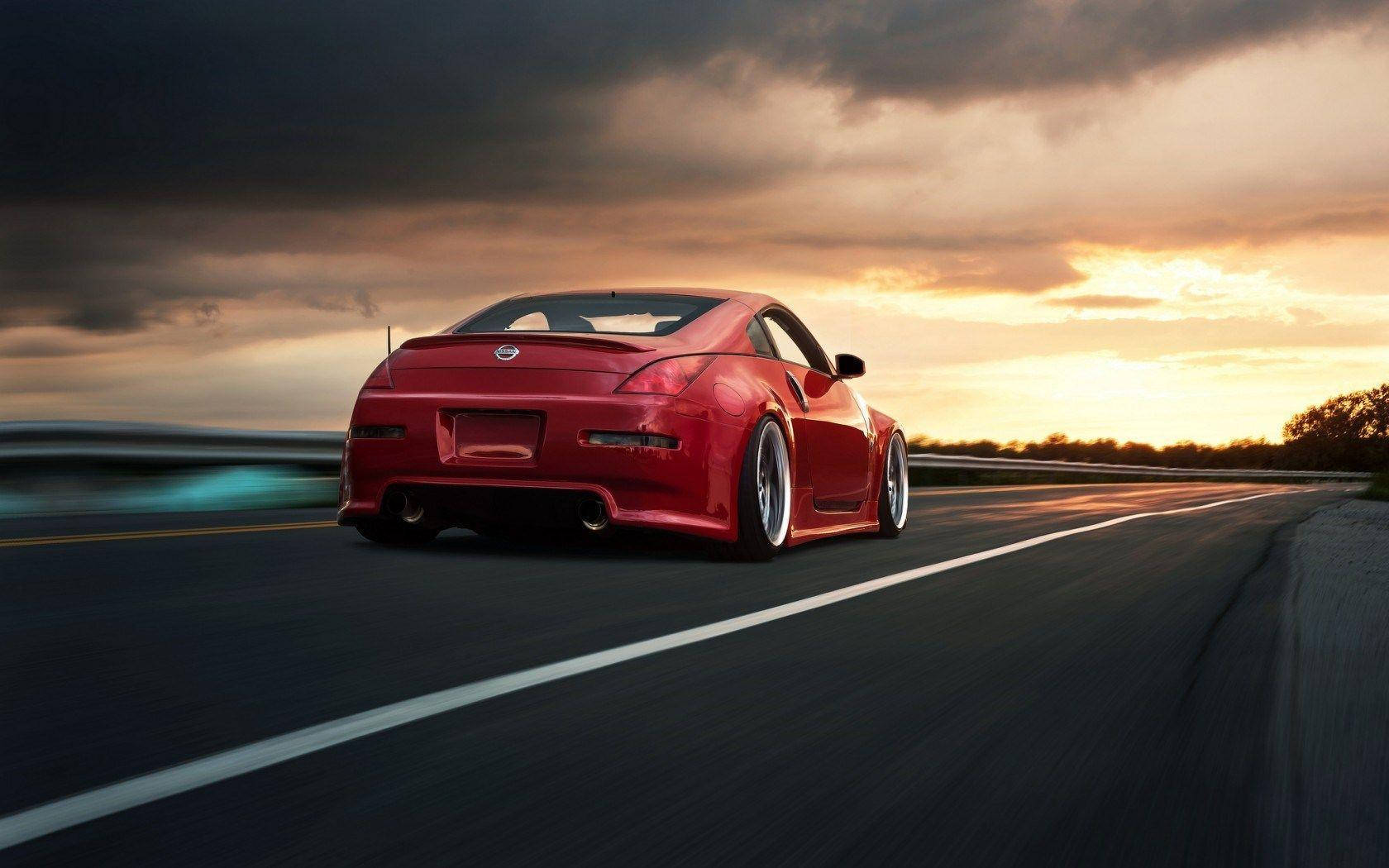 紅色 Nissan 350z iPhone 解鎖畫面 壁紙 — 一輛鮮紅色跑車在戲劇性的日落天空下，伴隨著動態模糊在高速公路上疾馳。