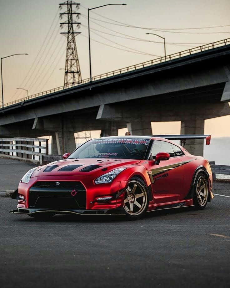 紅色 Nissan R35 GT-R 車圖 壁紙 — 一輛鮮紅色日產GT-R跑車，帶金色點綴，在黃昏時停泊在混凝土天橋下。