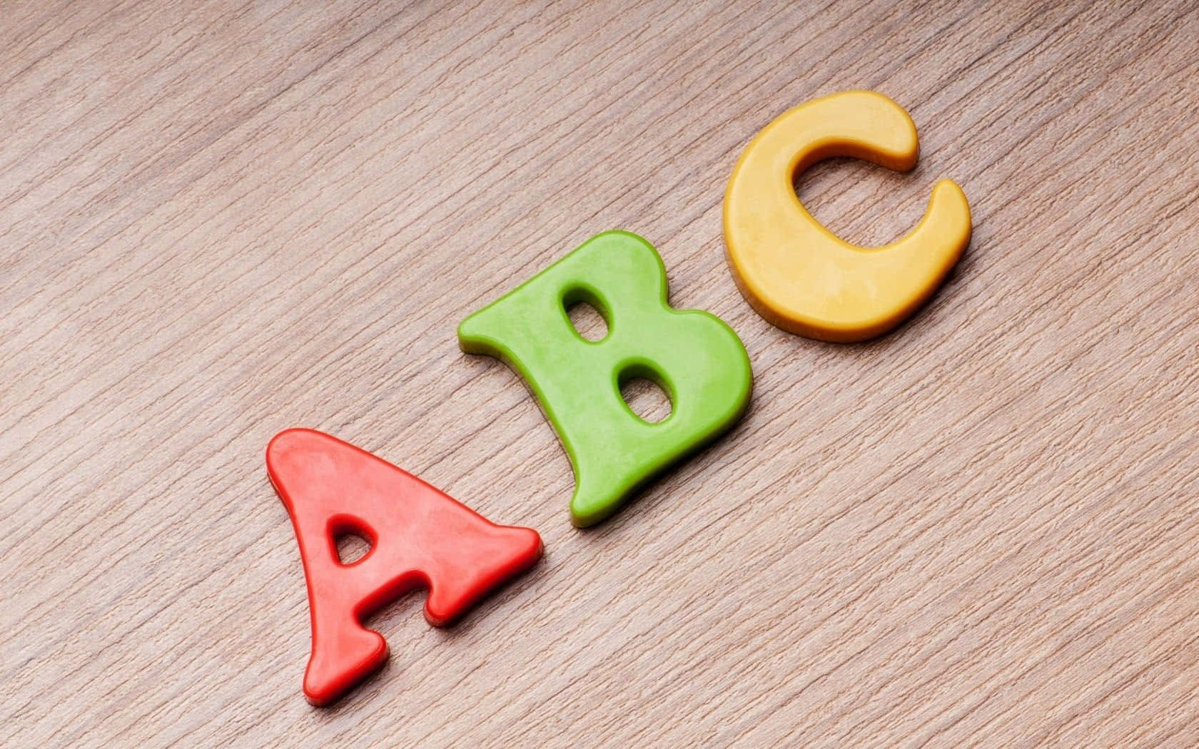 Abc 桌布 壁紙 — 紅色、綠色和黃色的黏土字母ABC以對角線排列在淺色木質表面上。