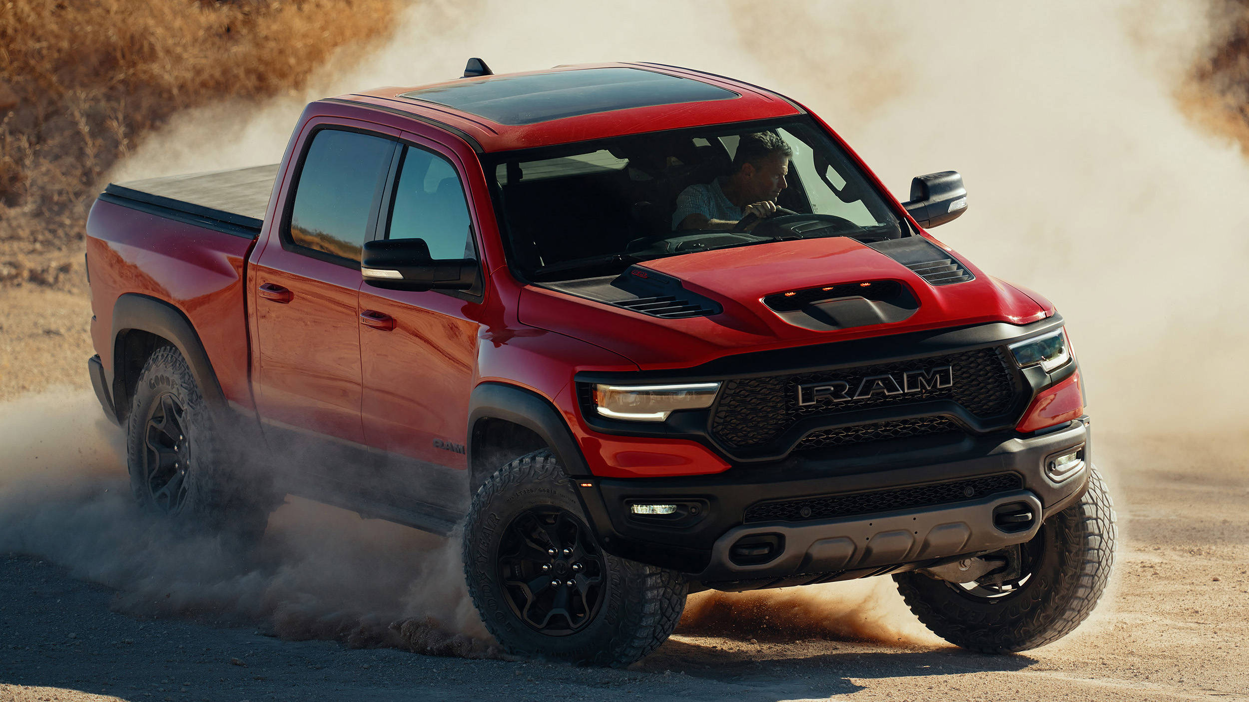 紅色2021 RAM卡車 壁紙 — 一輛紅色Ram pickup truck在明亮的日光下，在乾燥的泥路上疾馳，揚起灰塵。