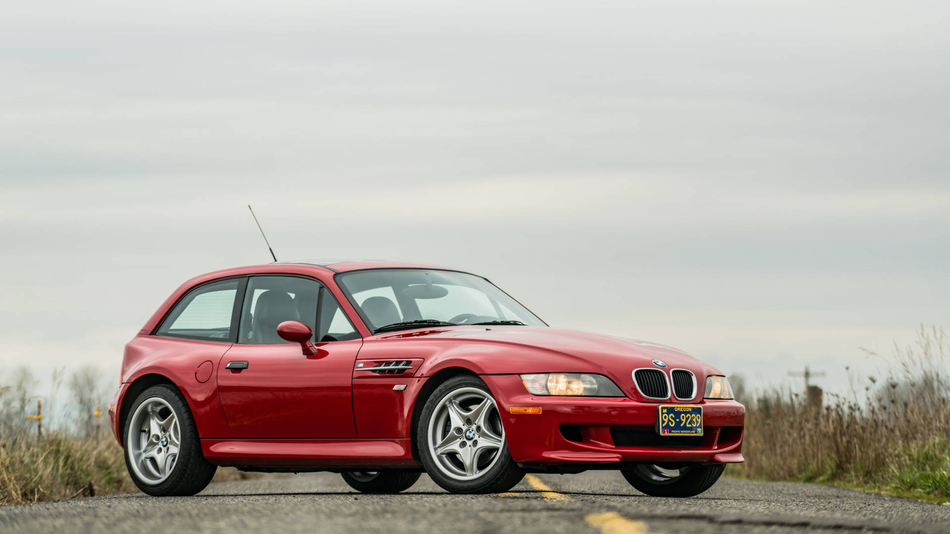紅色BMW Z3停泊在鄉郊路上，有乾草和多雲的天空。