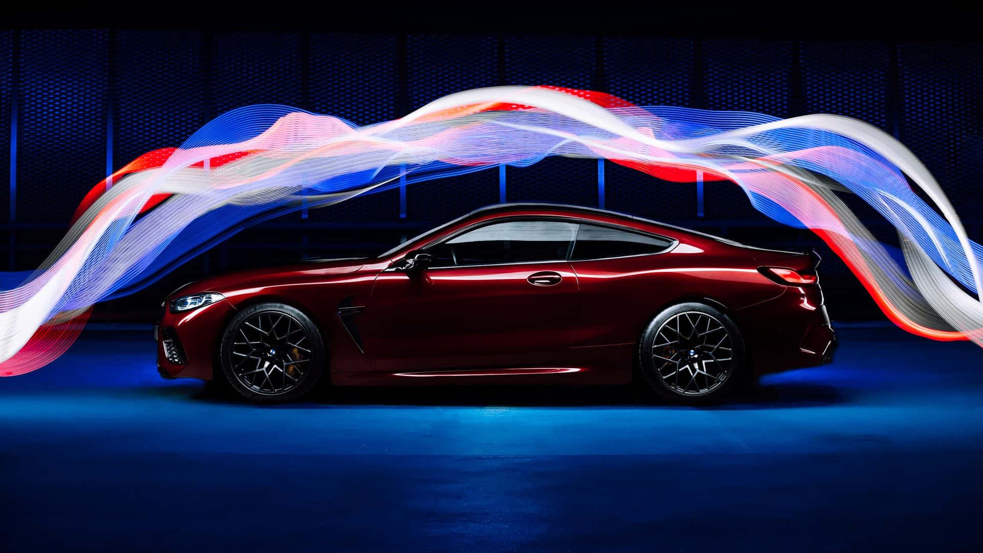 紅色BMW M8側面視角 1920x1080 M系列背景 壁紙 — 一輛流線型紅色跑車在黑暗的攝影棚中，於充滿活力的旋轉光跡下滑行。