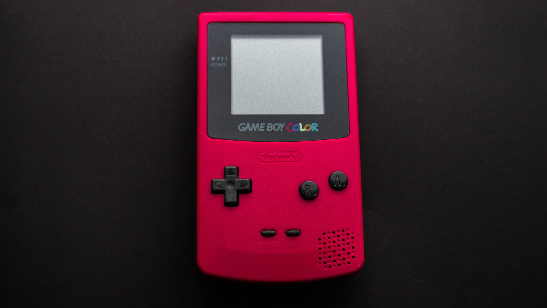紅色Game Boy Color置於黑色表面 壁紙 — 一部鮮粉紅色的Game Boy Color置於純黑背景中央，屏幕關閉，按鈕正等待遊戲。