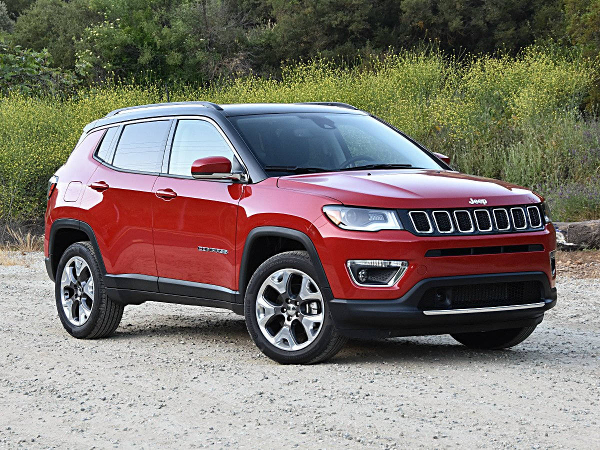 紅色Jeep Compass SUV停泊在碎石上，靠近綠色樹葉。