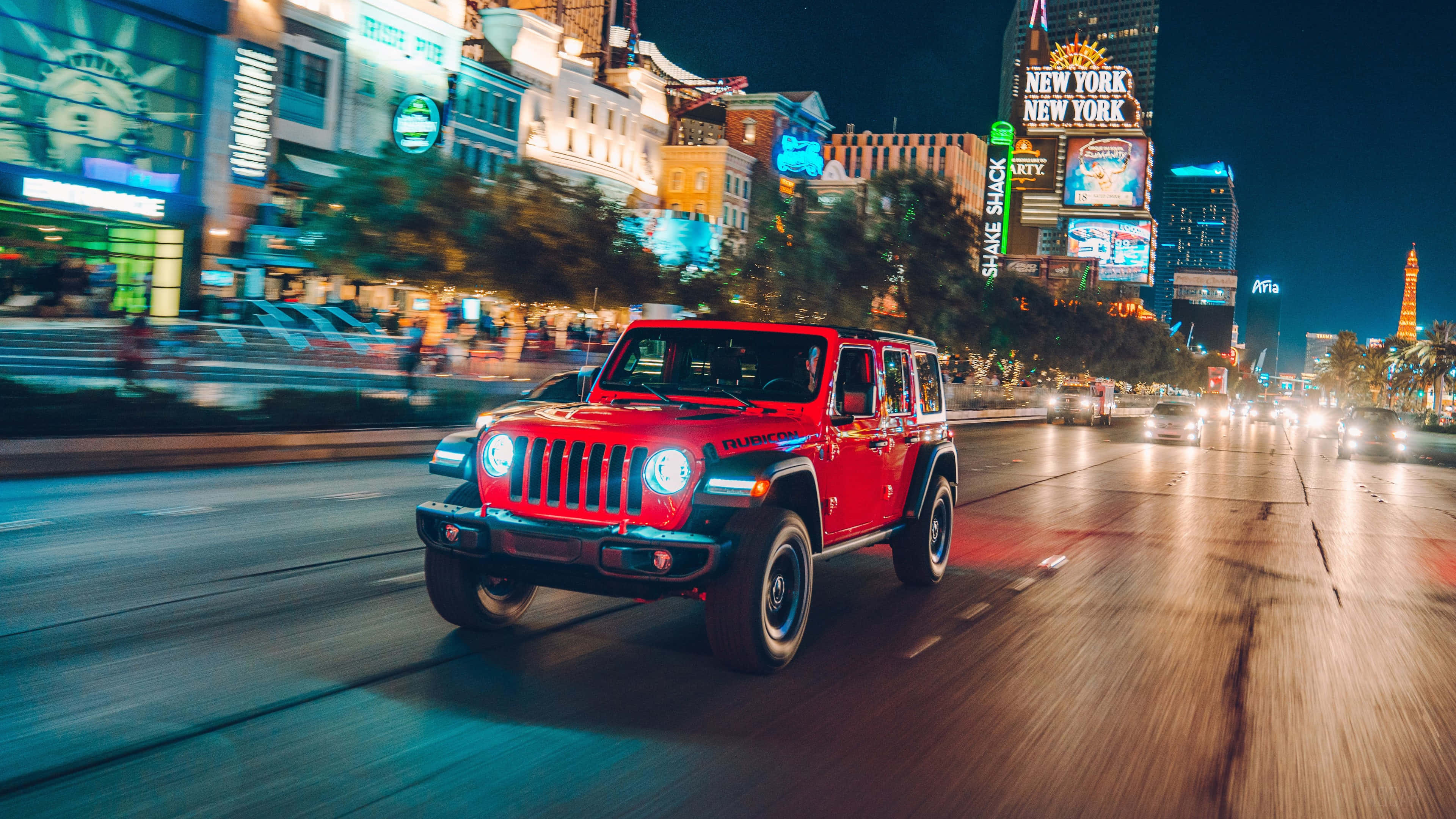 紅色Jeep Wrangler在夜晚城市街道上行駛 壁紙