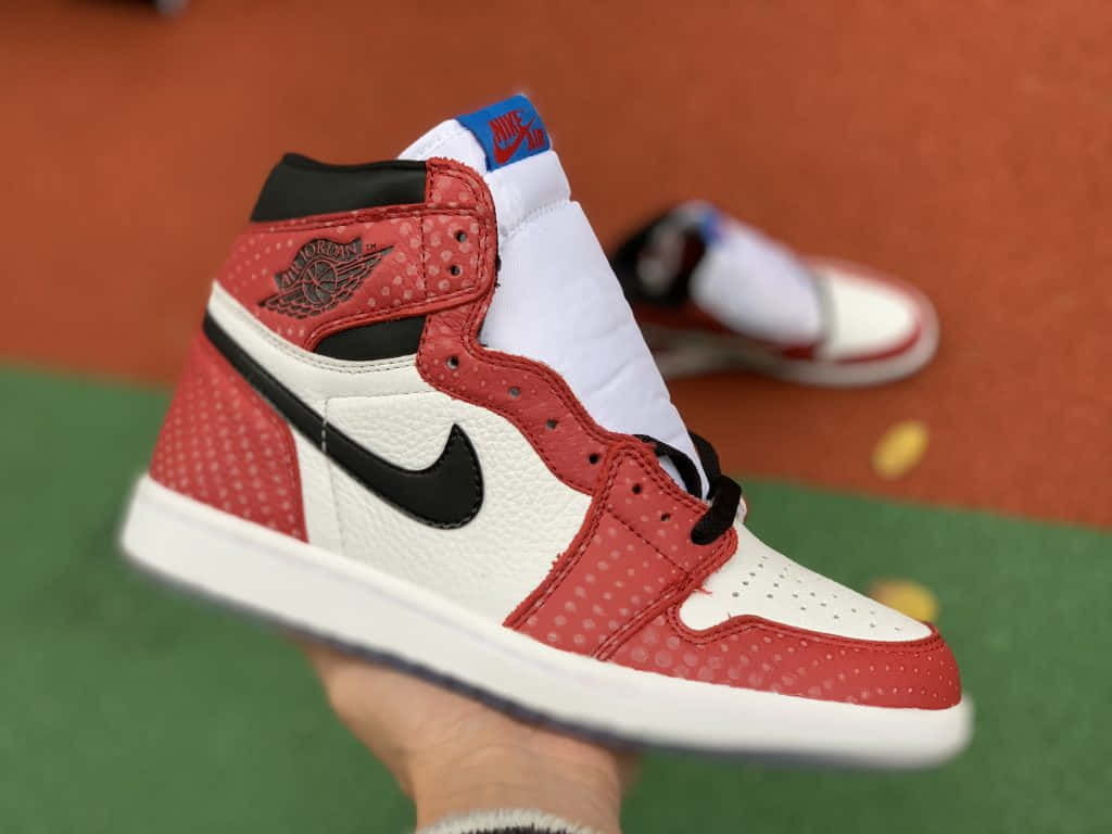 在網球場上，一隻手拿著一雙紅白黑配色的Jordan 1運動鞋。