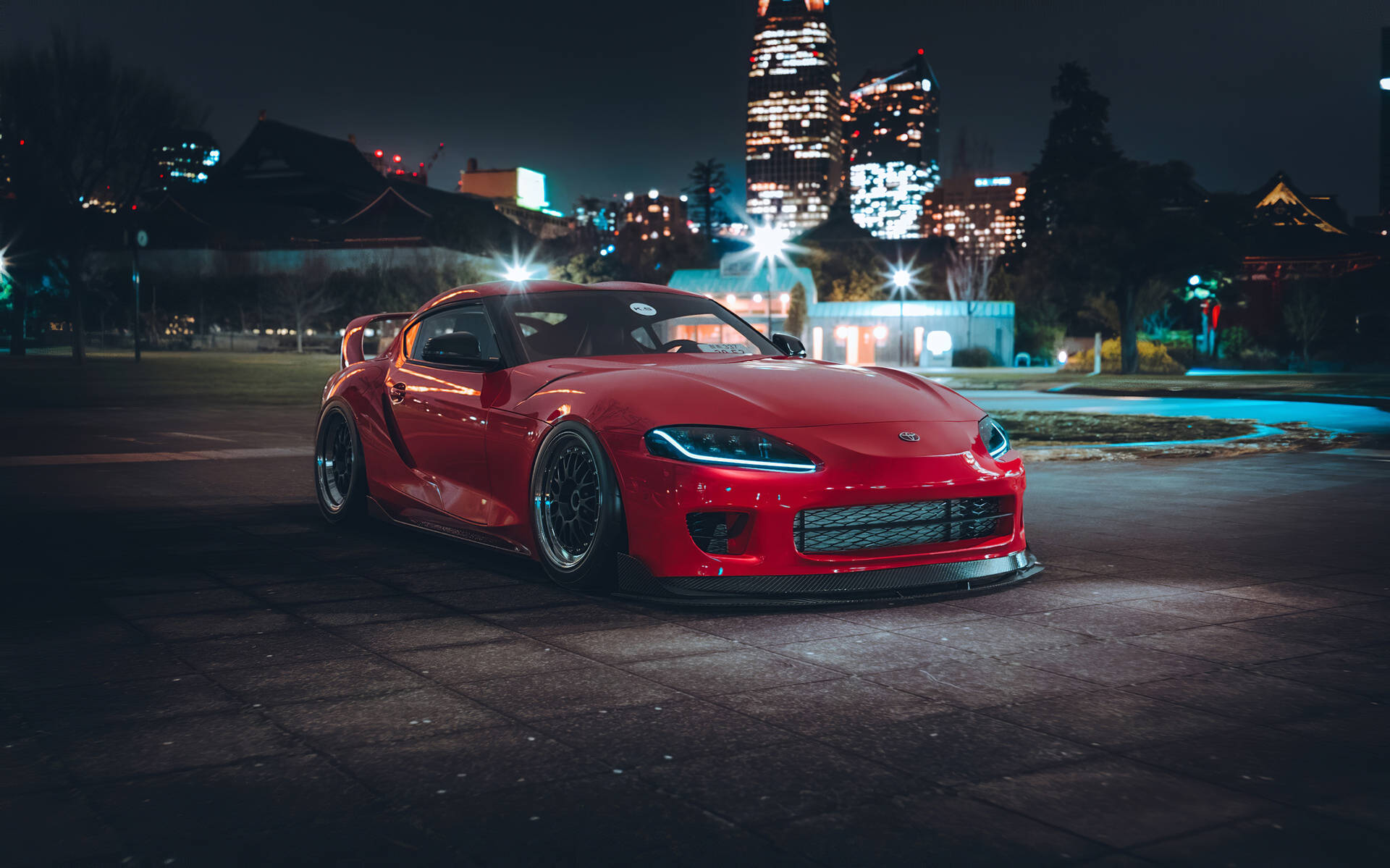 紅色跑車夜間停放，背景有城市燈光