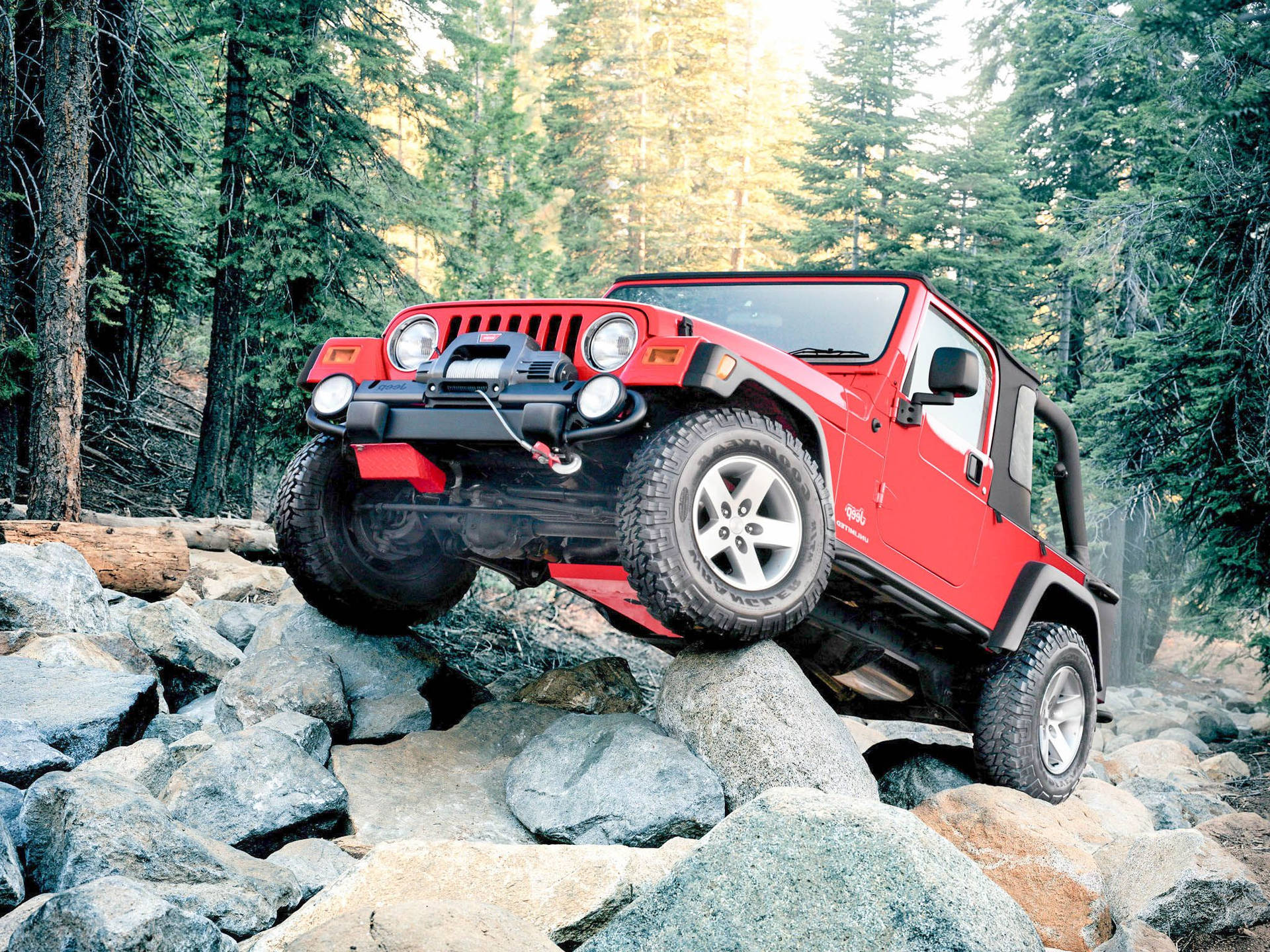 紅色Jeep Wrangler在森林中攀爬大岩石。