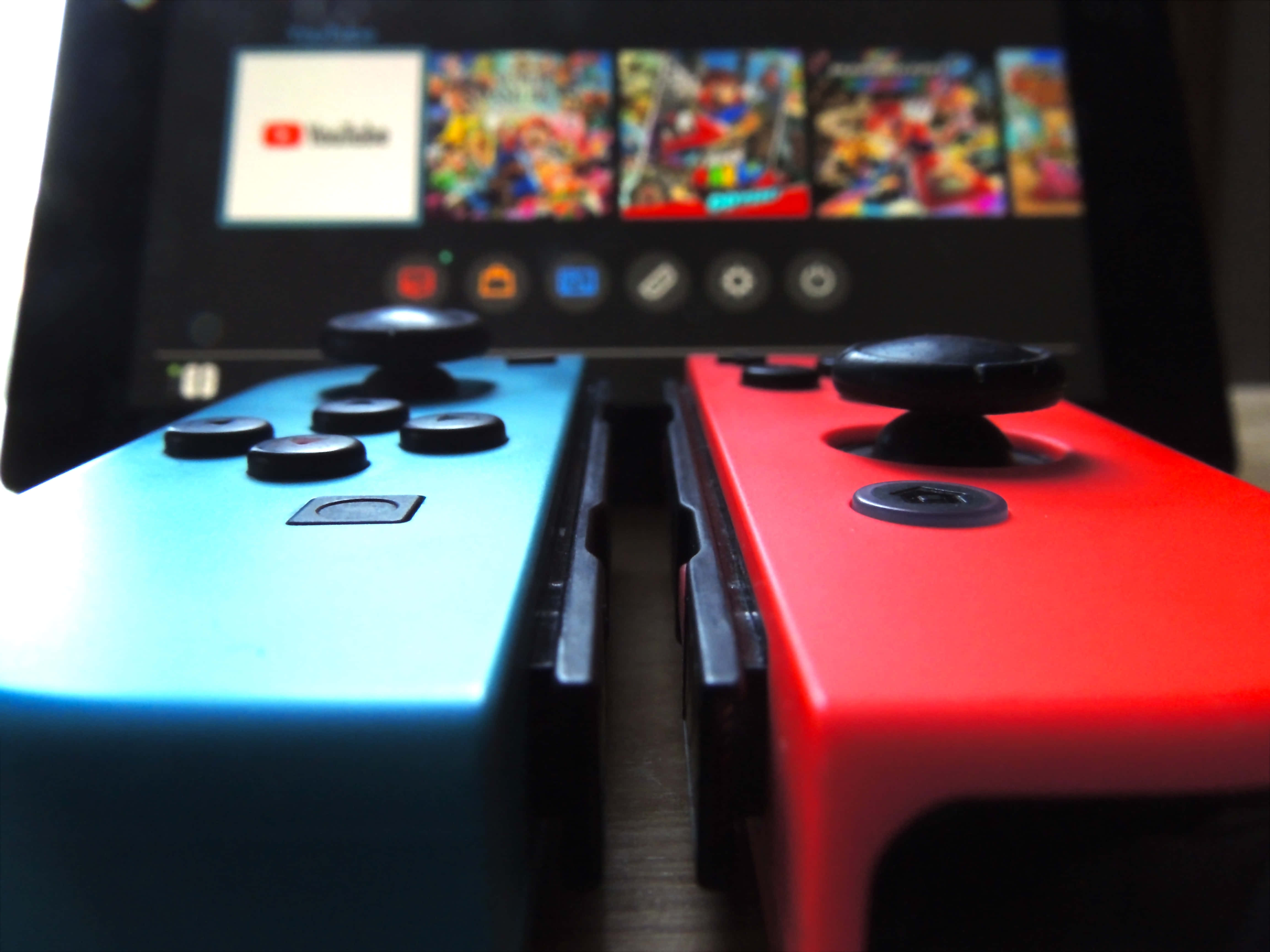 Gaming Consoles 桌布 壁紙 — 紅色和藍色 Nintendo Switch Joy-Con 的特寫，背景有模糊的遊戲畫面。