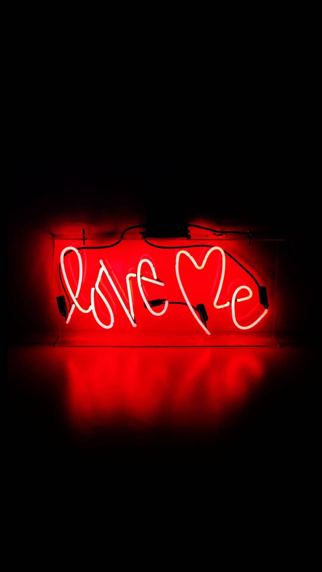 紅色壞女孩 愛我 壁紙 — 一個發光的紅色霓虹燈牌，拼出「Love Me」，並以心形取代字母「o」，在黑暗的表面上投射出溫暖的倒影。
