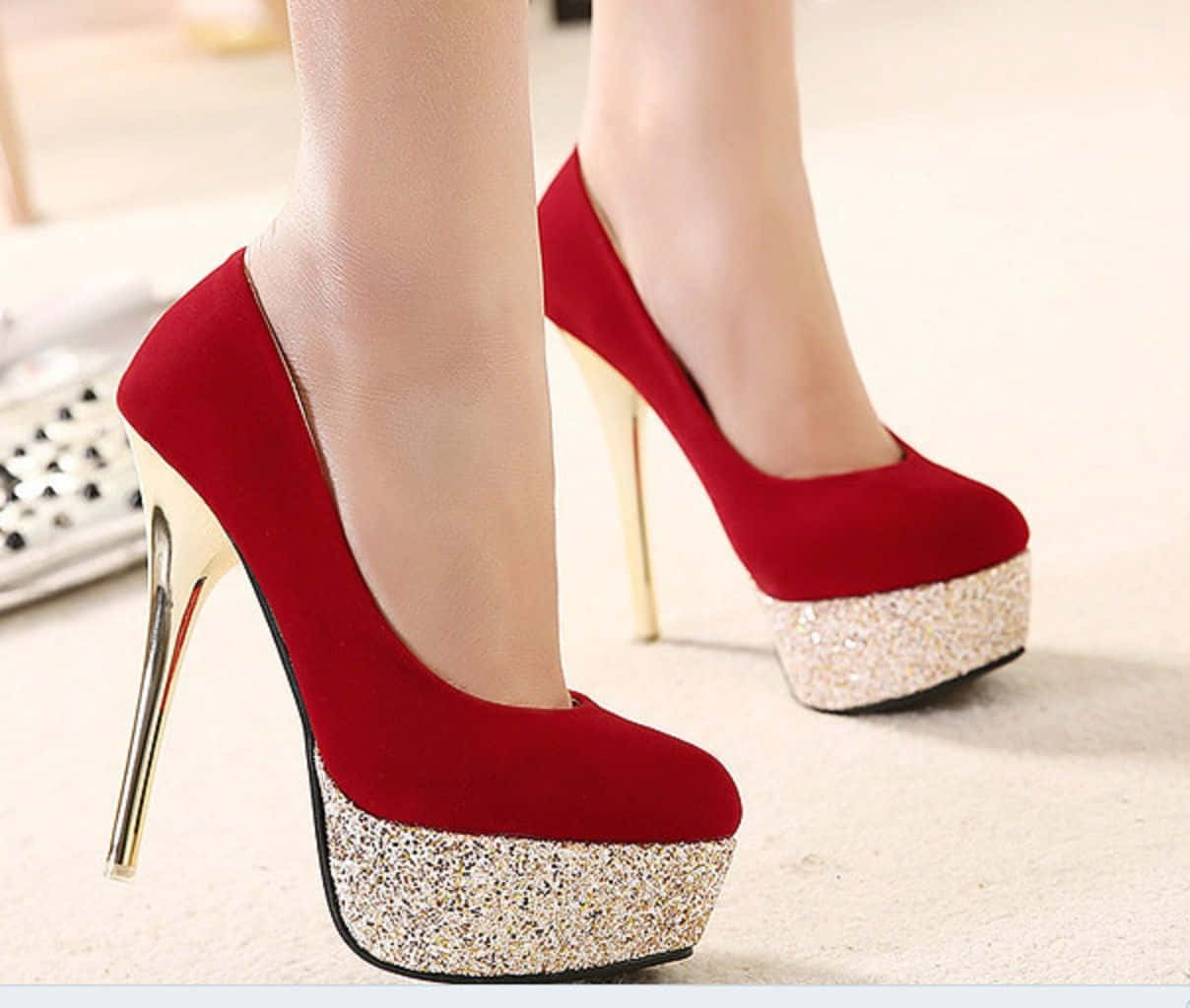Red High Heels 桌布 壁紙 — 紅色天鵝絨厚底高跟鞋，配金色細高跟和閃亮鞋底，由一位站在淺色地板上的人穿著。