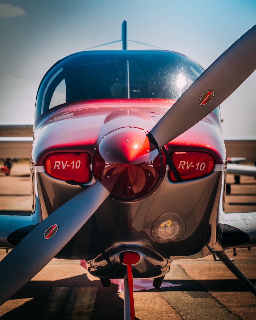 紅色小型飛機螺旋槳 壁紙 — 晴朗停機坪上紅銀色RV-10飛機機頭和螺旋槳的特寫，背景是清澈的藍天。