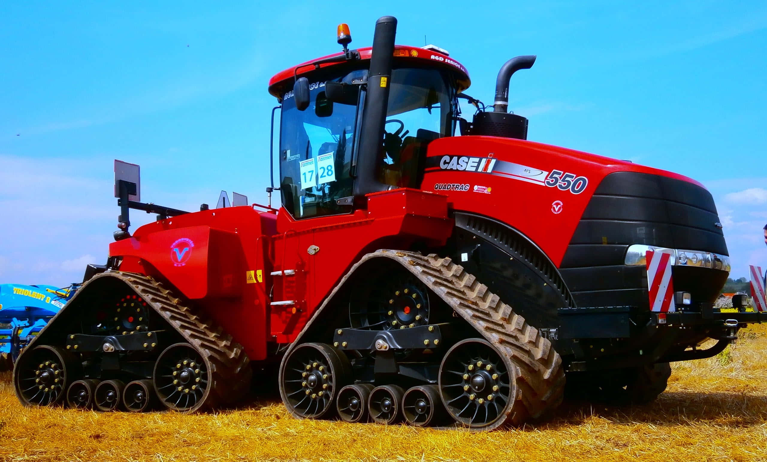紅色巨型拖拉機 壁紙 — 一台鮮紅色的Case IH 550履帶拖拉機在晴朗的藍天下，醒目地矗立在金色的乾草田上。