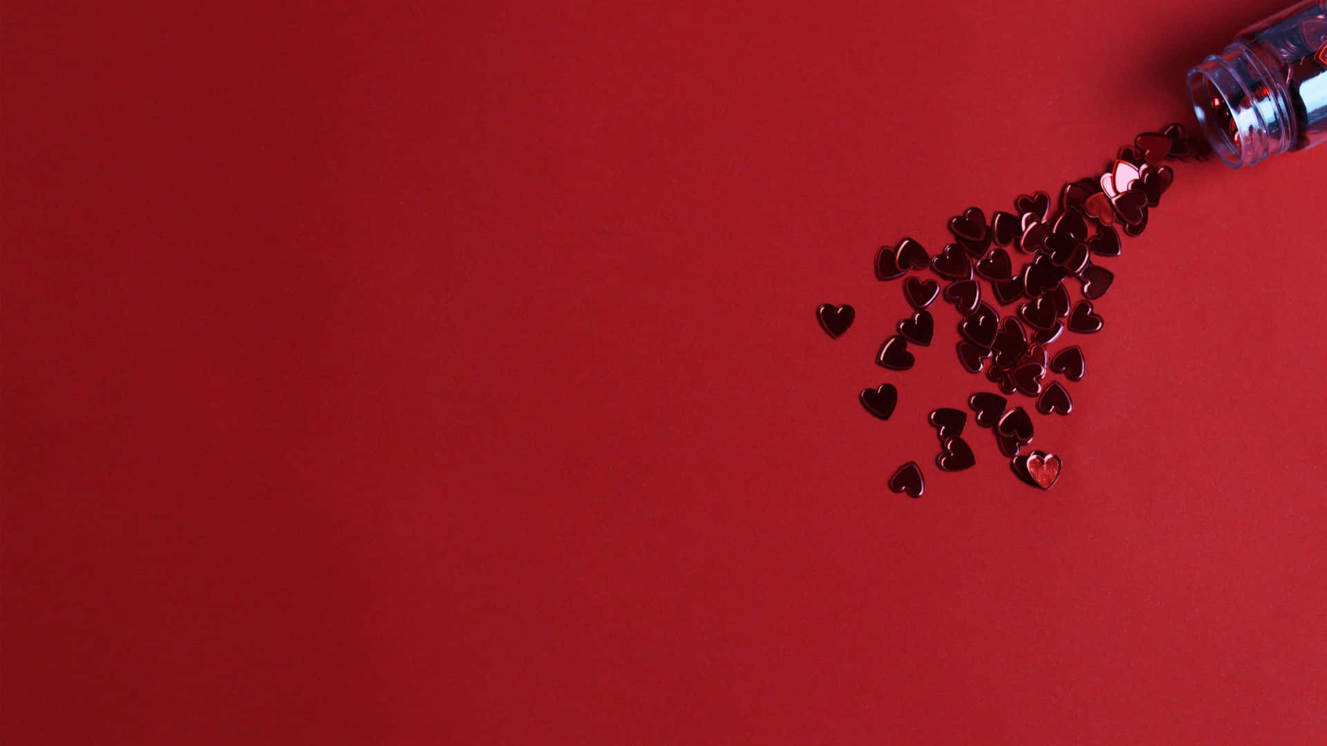 紅色心形紙屑從瓶子中灑落在紅色背景上。