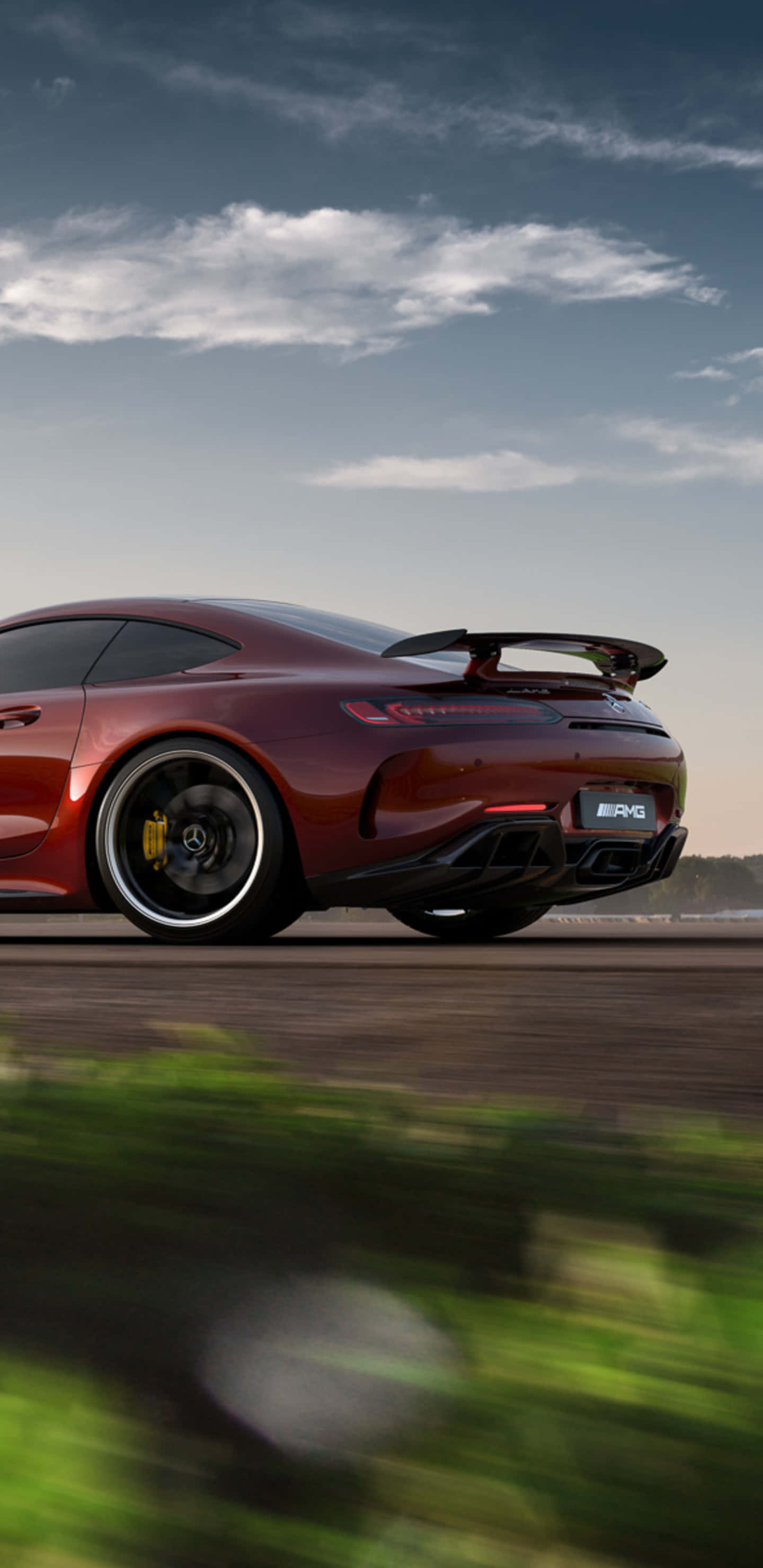 紅色梅賽德斯-奔馳配尾翼 Pixel 3XL AMG GT-R 背景 壁紙 — 一輛酒紅色的 Mercedes-AMG GT R 跑車在道路上疾馳，背景是模糊的綠植和多雲的天空。