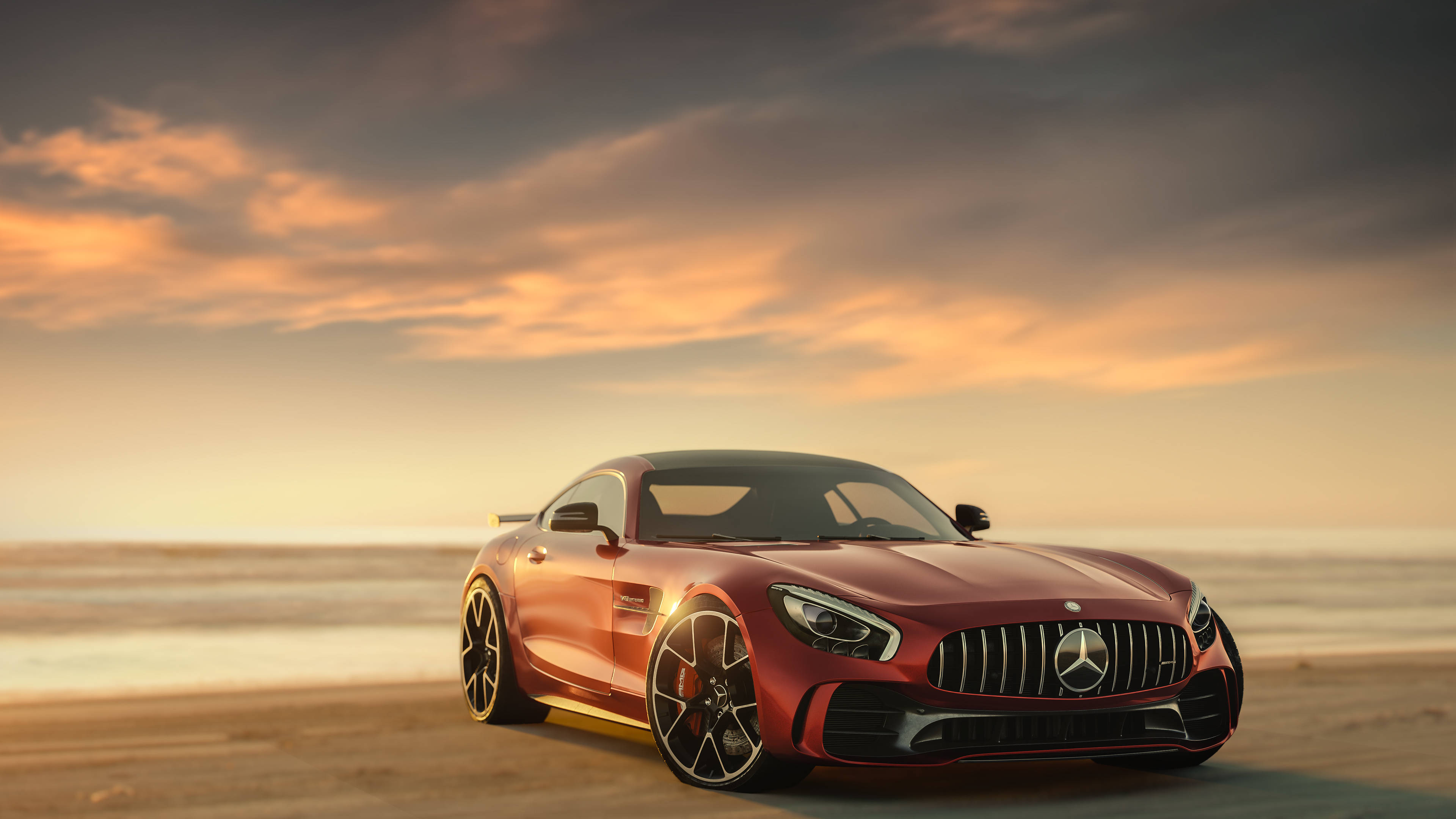 紅色梅賽德斯AMG海灘日落 壁紙 — 一架時尚的紅色 Mercedes-AMG GT 跑車停泊在日落時分的沙灘上，上方有金色雲彩。
