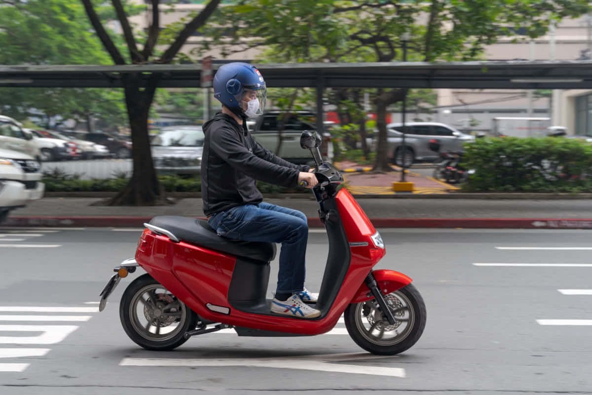 喺城市街道上騎紅色滑板車嘅人，背景有樹木同汽車。