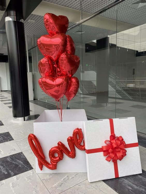 現代玻璃建築大堂中的紅色心形和「love」氣球與禮品盒。