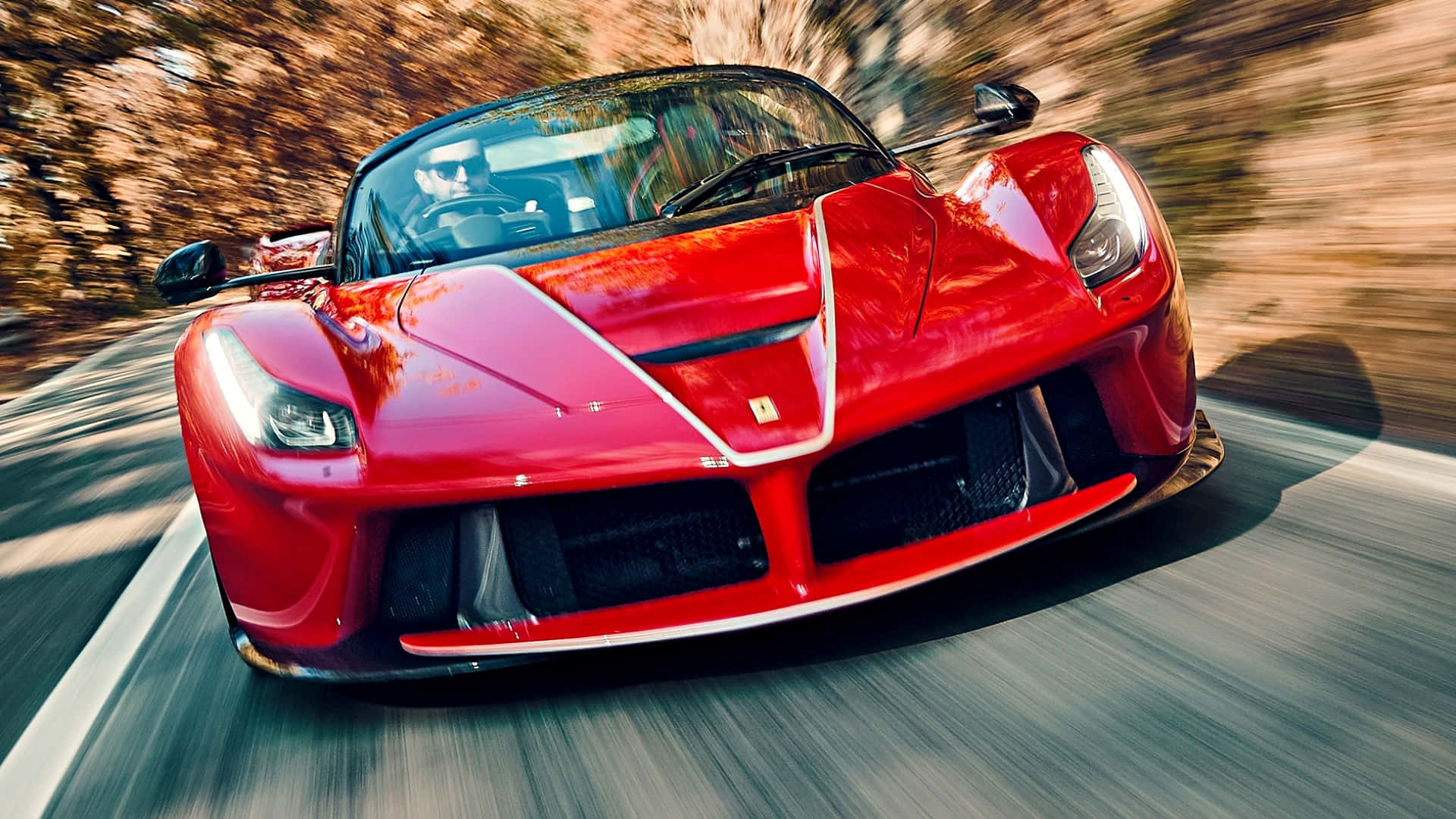 紅色法拉利 LaFerrari 在蜿蜒道路上奔馳，秋樹呈現動態模糊。