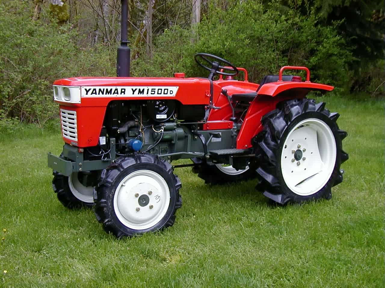 紅色洋馬拖拉機田間風景 壁紙 — 一輛白色車輪的鮮紅色Yanmar YM1500D拖拉機，站在茂密樹木環繞的翠綠草地上。