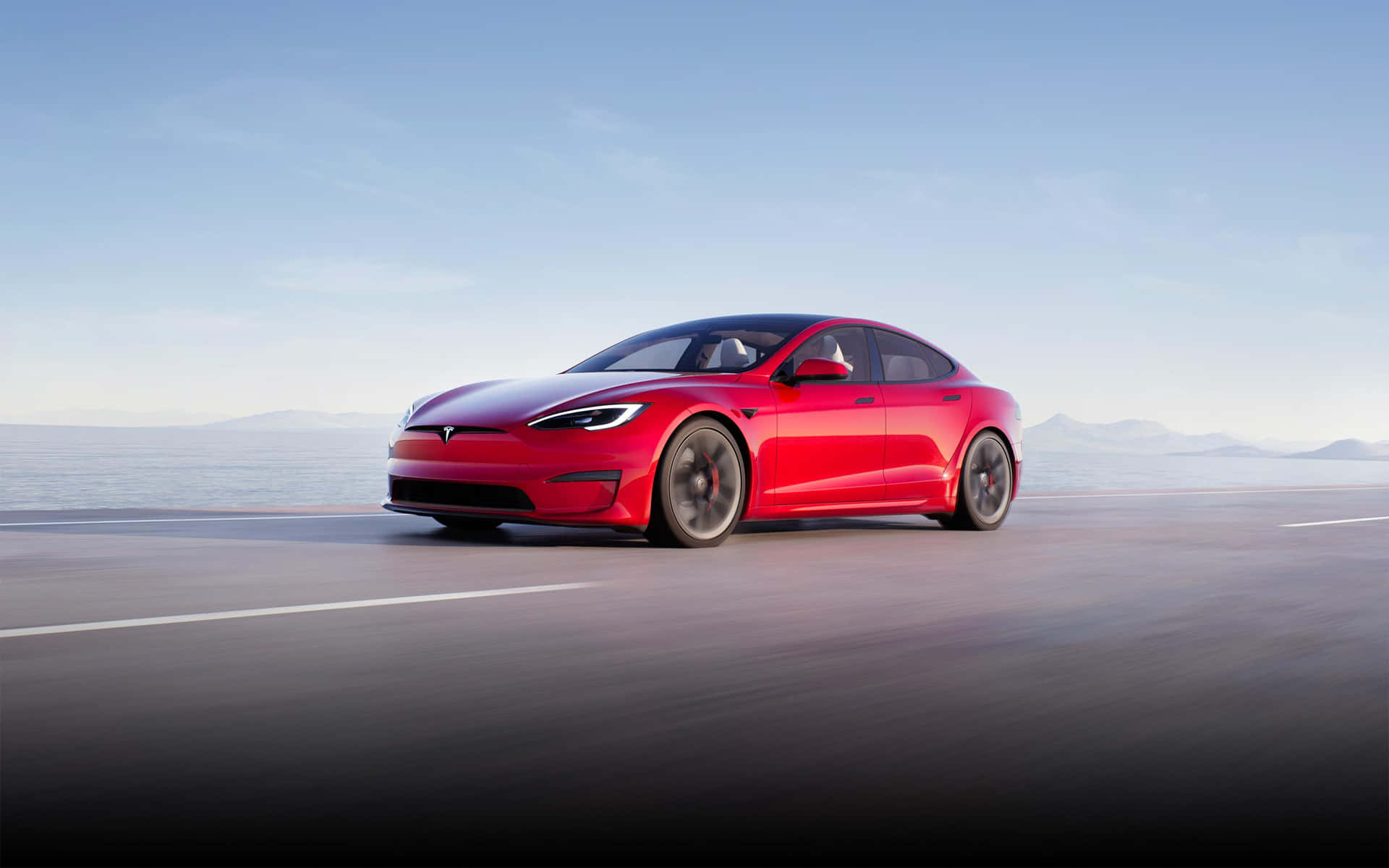 紅色Tesla Model S在日落時分行駛在海岸公路上，背景有山巒。