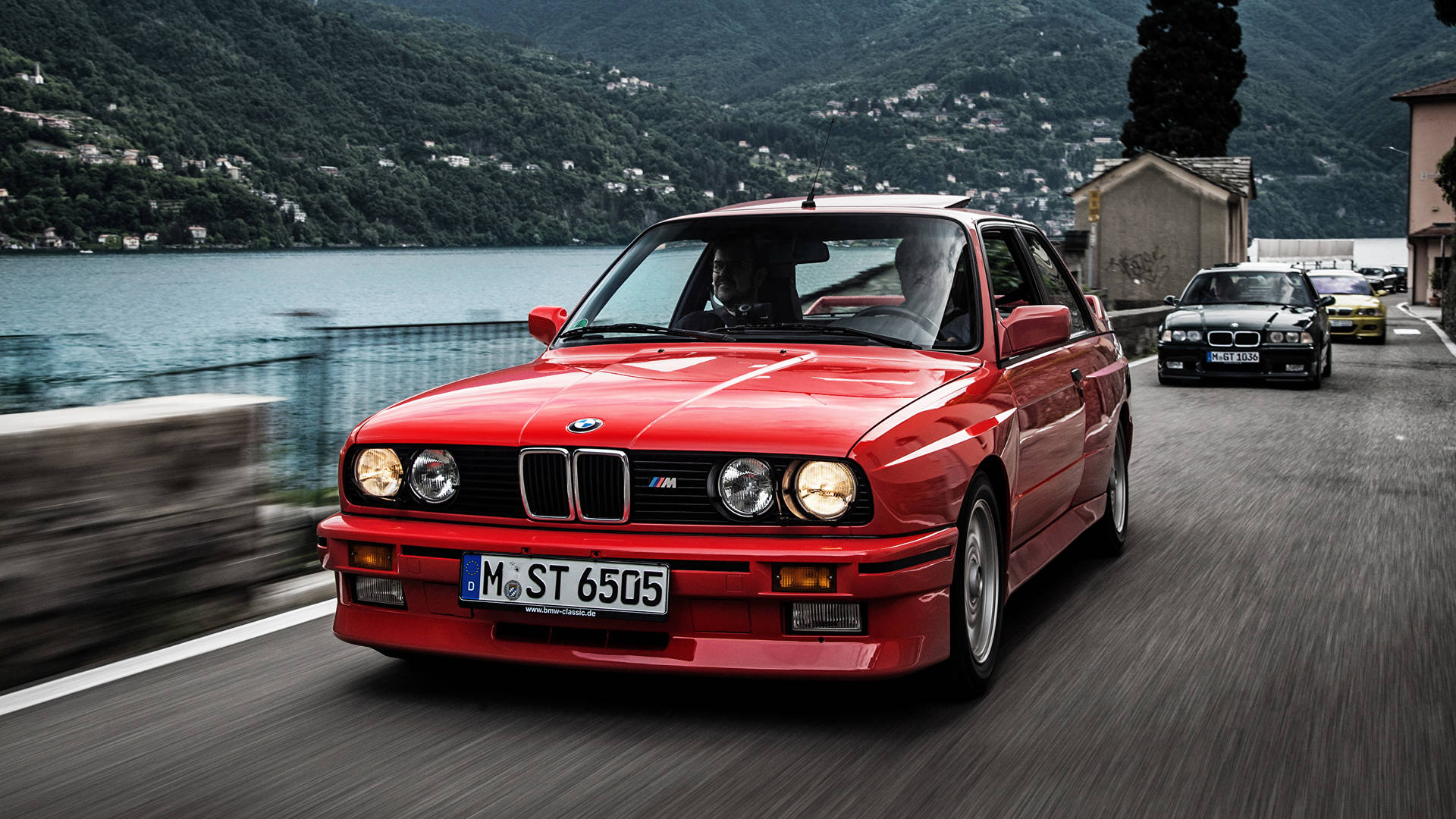 紅色BMW M3在風景如畫的湖邊道路上疾馳，帶有動態模糊效果。
