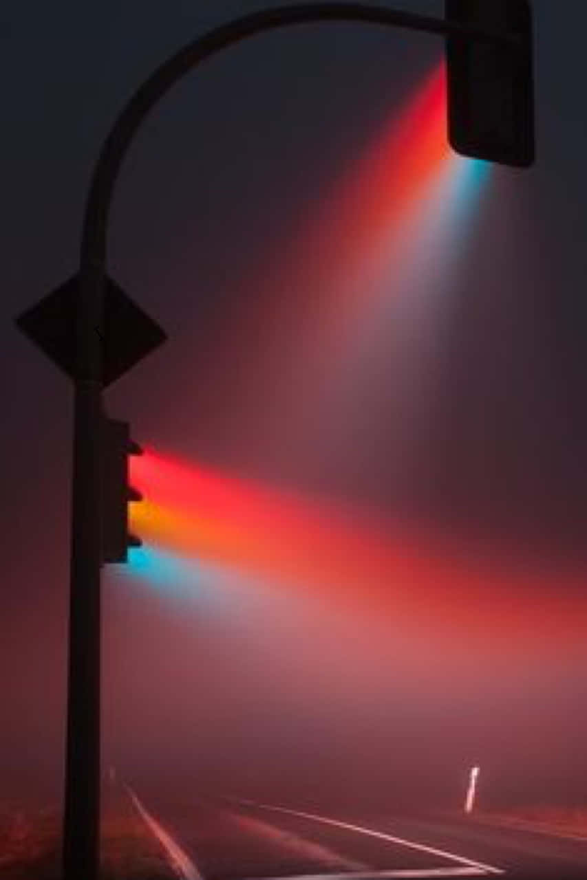 交通燈光束在夜晚黑暗的道路上穿透霧氣。
