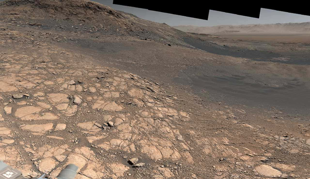 探測車在塵土飛揚的天空下探索裂開的岩石火星表面。