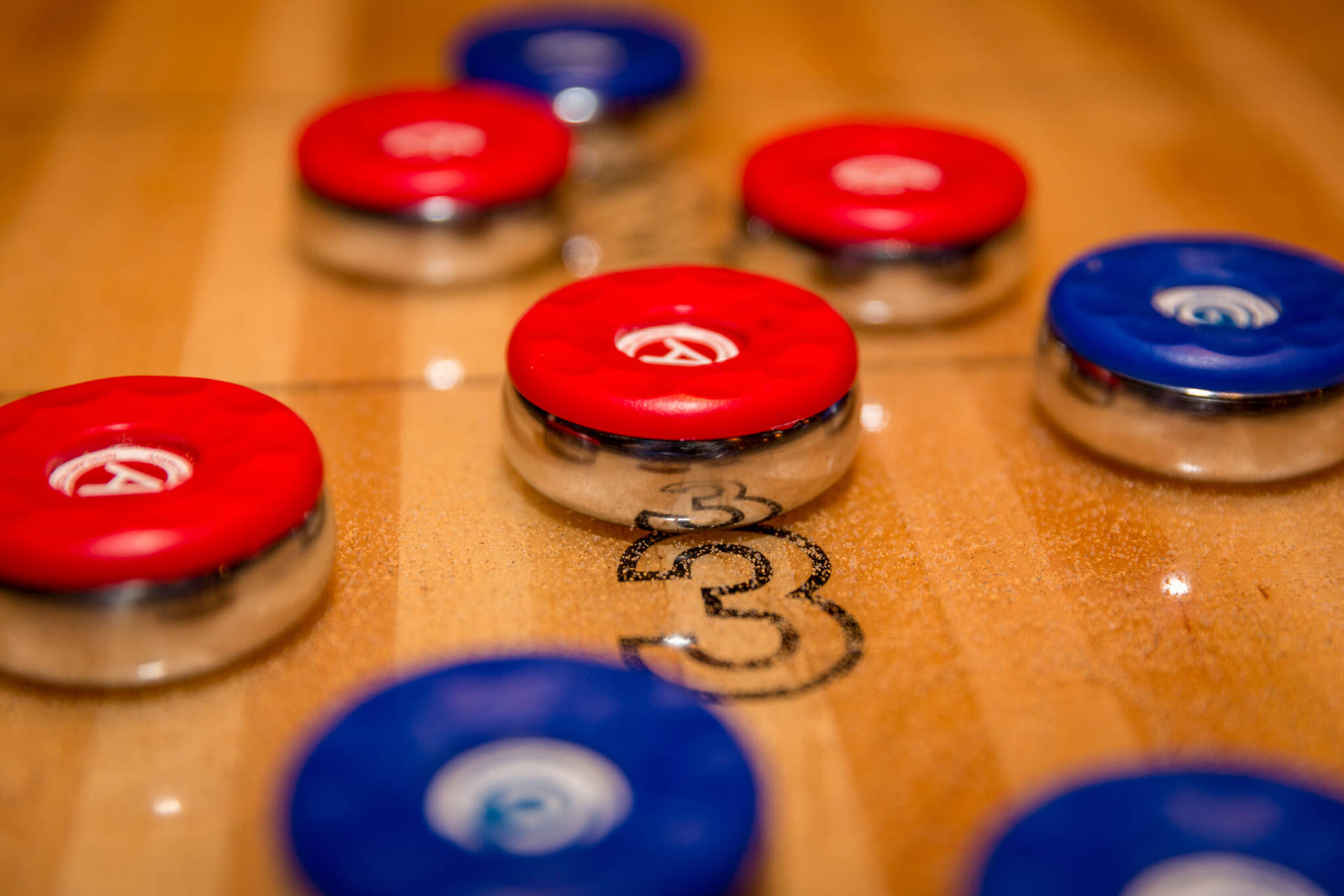 紅色遊戲盤 Shuffleboard 宏觀特寫 壁紙 — 木製冰壺場上紅色和藍色冰壺石的特寫，帶有可見的計分標記。