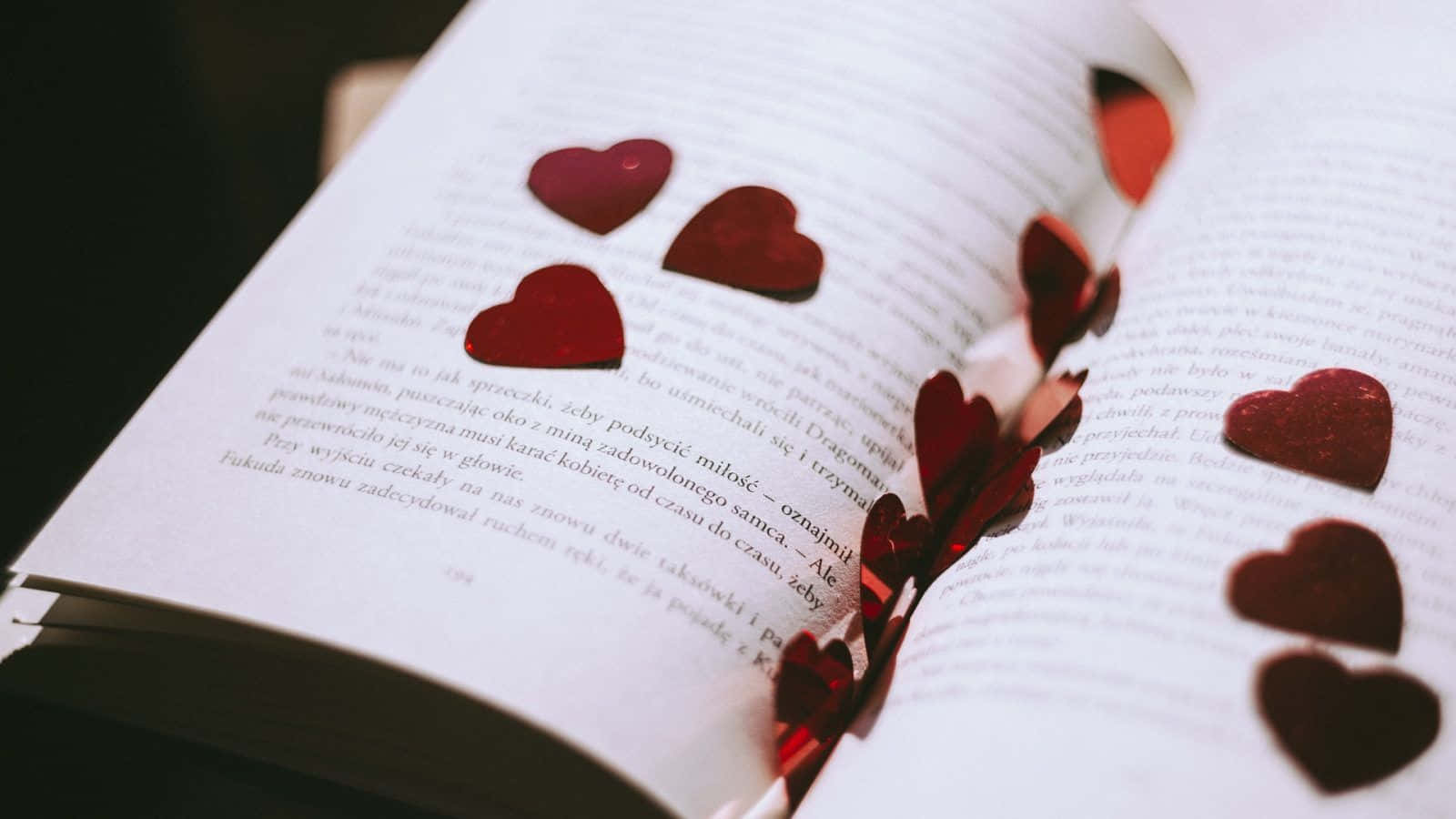 Romance Literature 桌布 壁紙 — 紅色閃亮心形散落在打開的書頁上，背景柔和模糊。