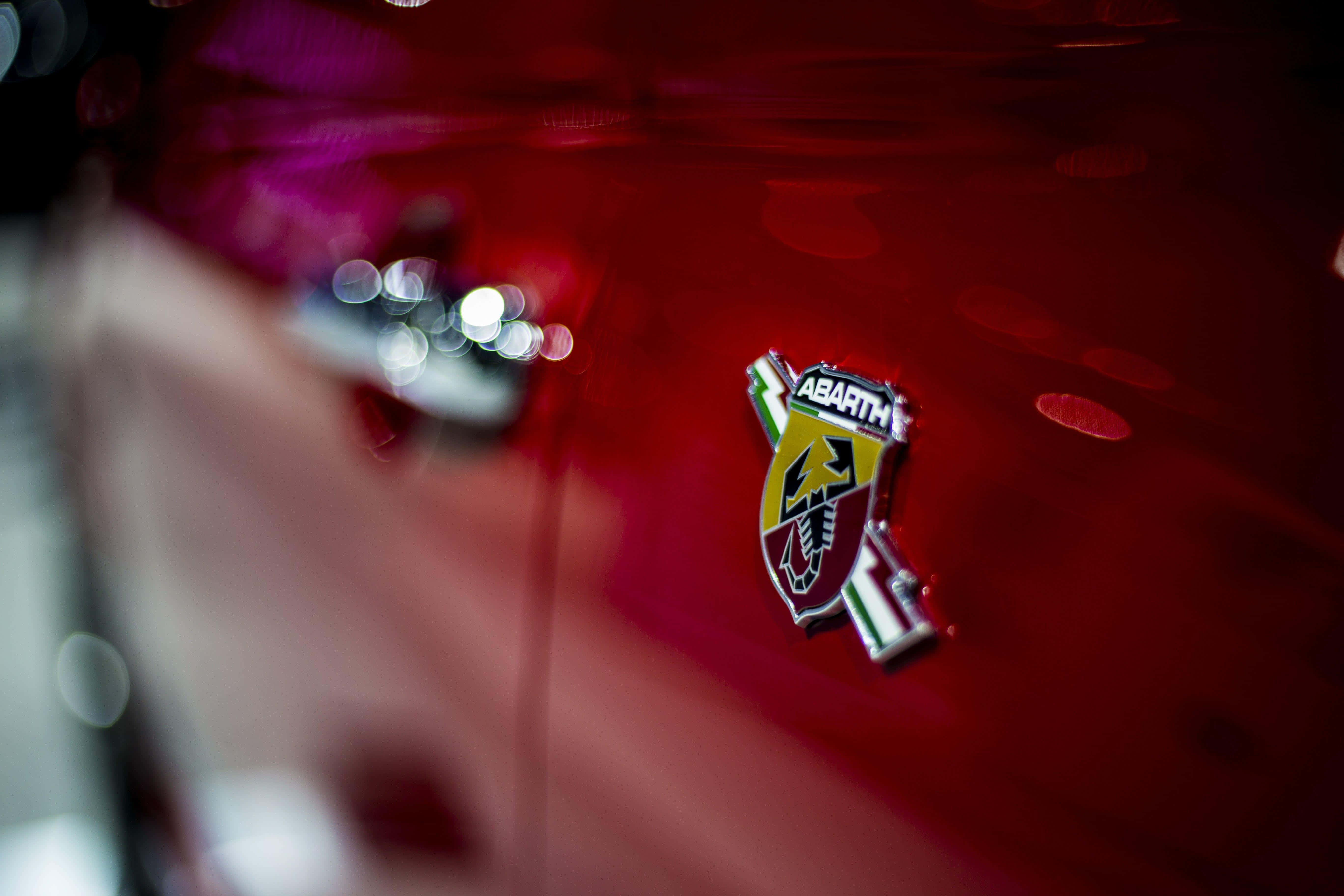 Abarth 桌布 壁紙 — 紅色閃亮汽車引擎蓋的特寫，帶有標誌性的 Abarth 徽章，上面有蠍子和意大利三色條紋。