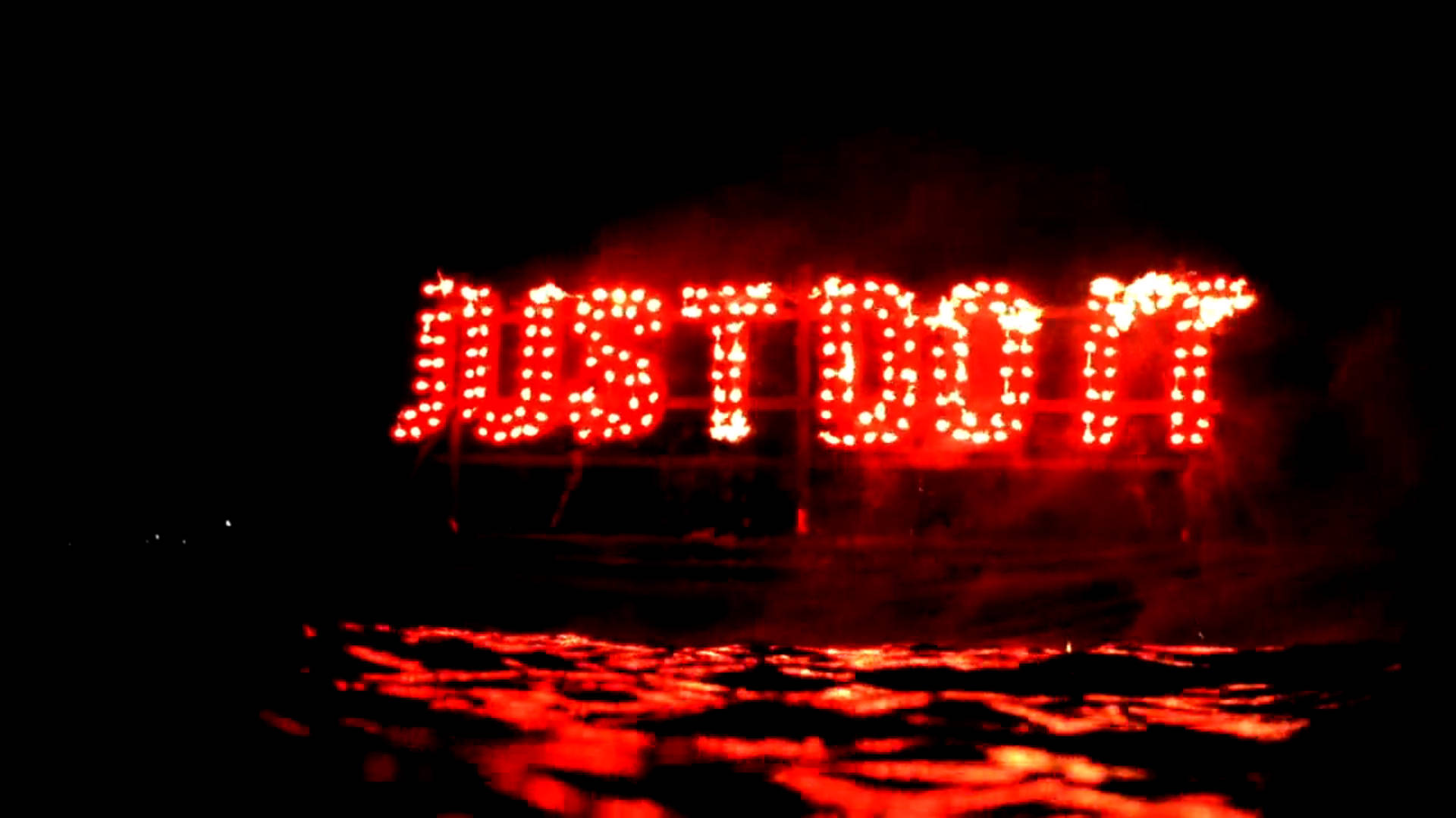 紅色霓虹「Just Do It」招牌 壁紙 — 大膽的紅色LED字母拼出JUST DO IT，在黑暗的夜空中強烈發光，下方濕漉漉的地面上反射出閃爍的光芒。