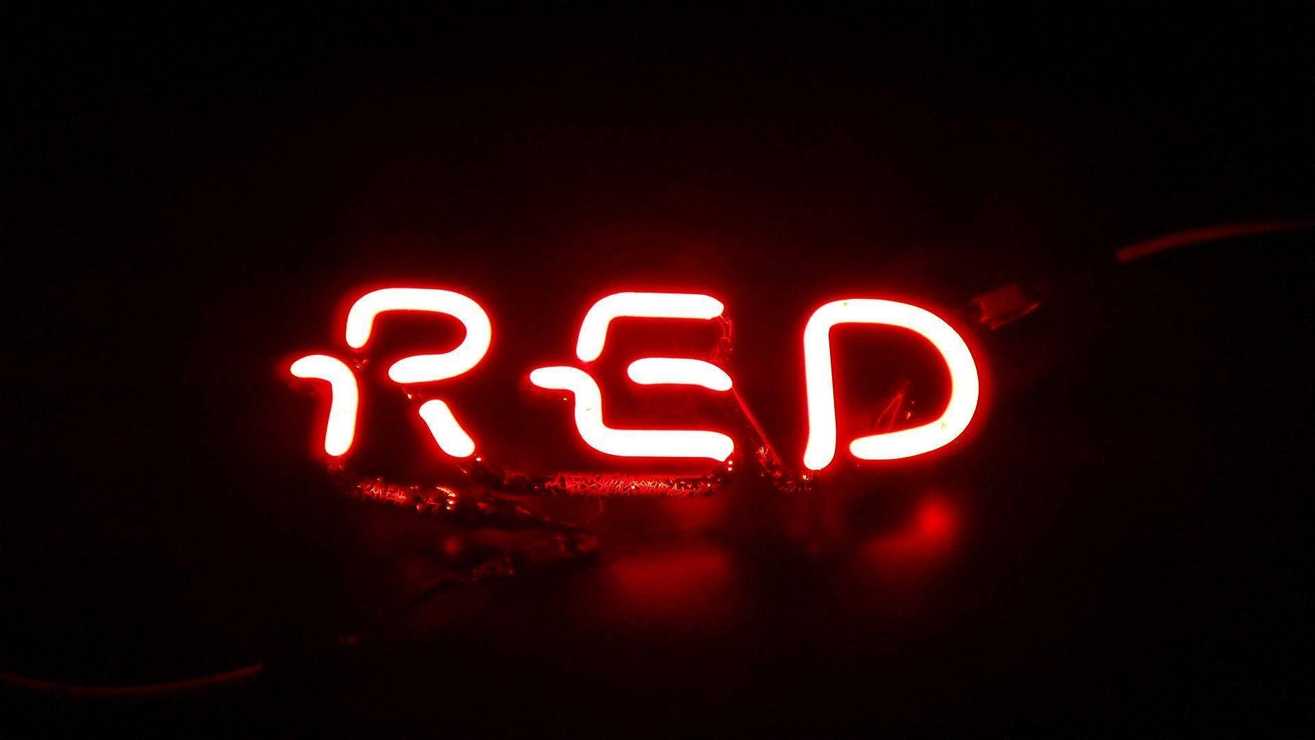 紅色霓虹文字燈光 壁紙 — 一個發光的紅色霓虹燈牌，拼寫著「RED」，在漆黑的背景下明亮地閃耀。