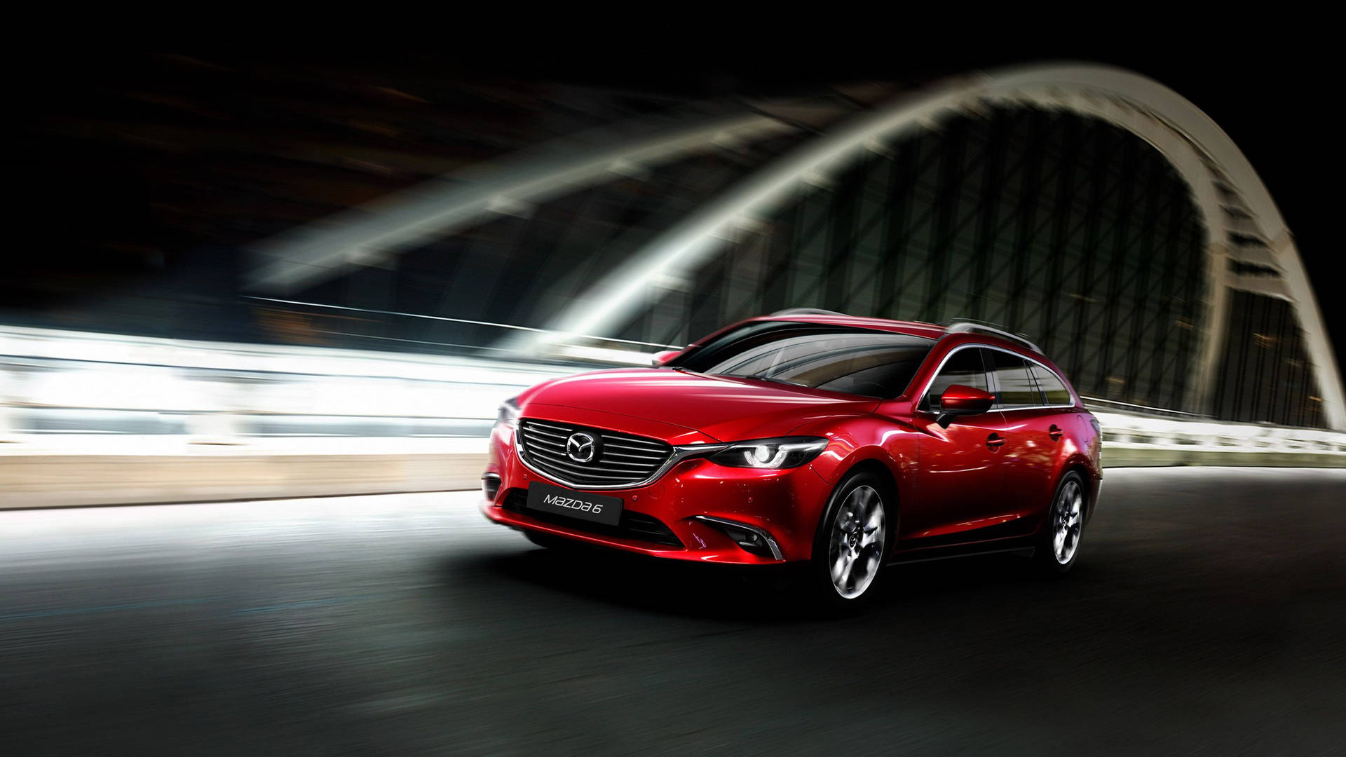 紅色Mazda6旅行車在夜間於燈光拱橋下疾馳。