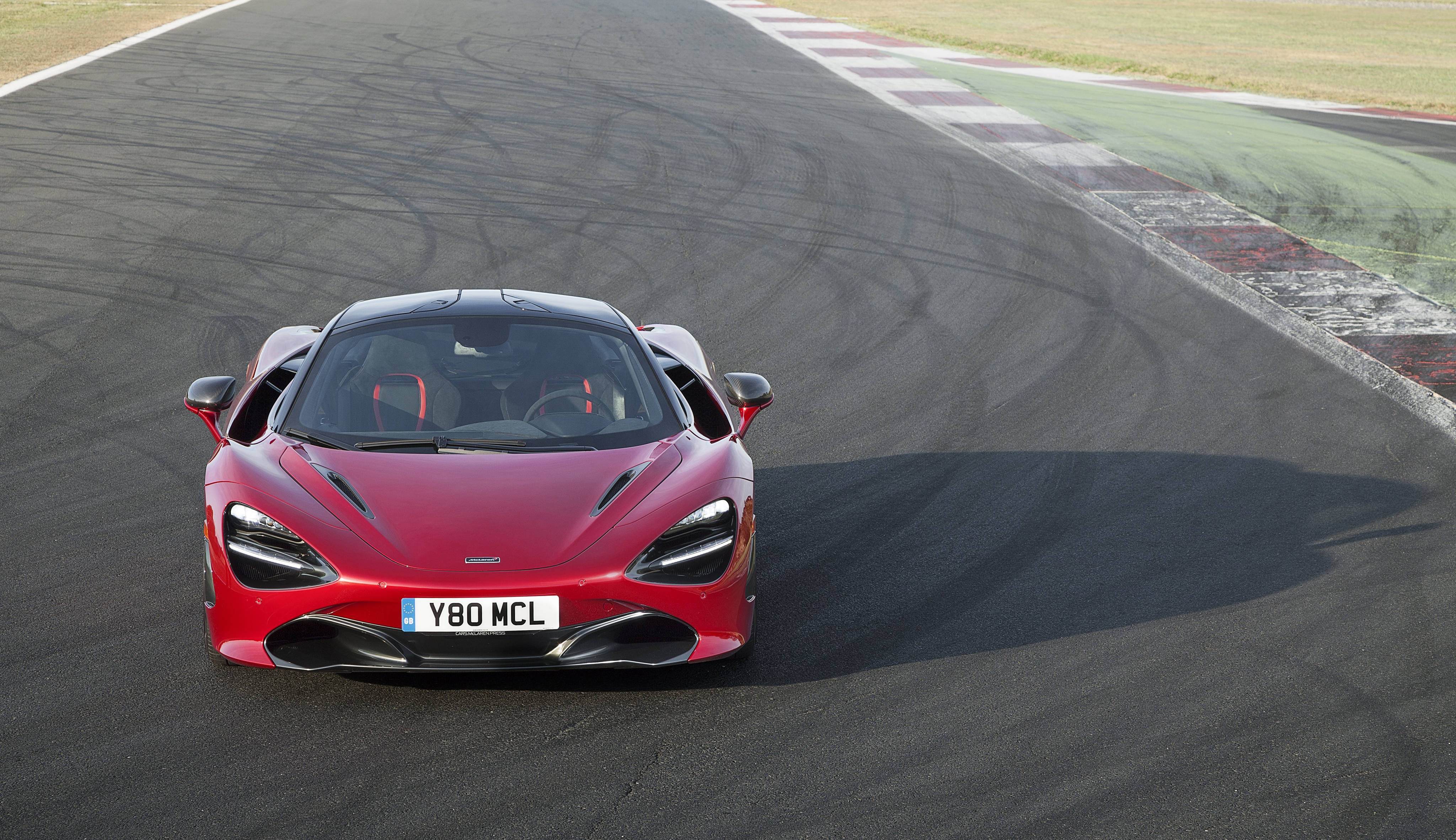 紅色麥拉倫720S 4K前視圖 壁紙 — 一輛鮮紅色的McLaren 720S跑車在明亮的日光下沿著賽道飛馳，輪胎痕跡和路緣清晰可見。