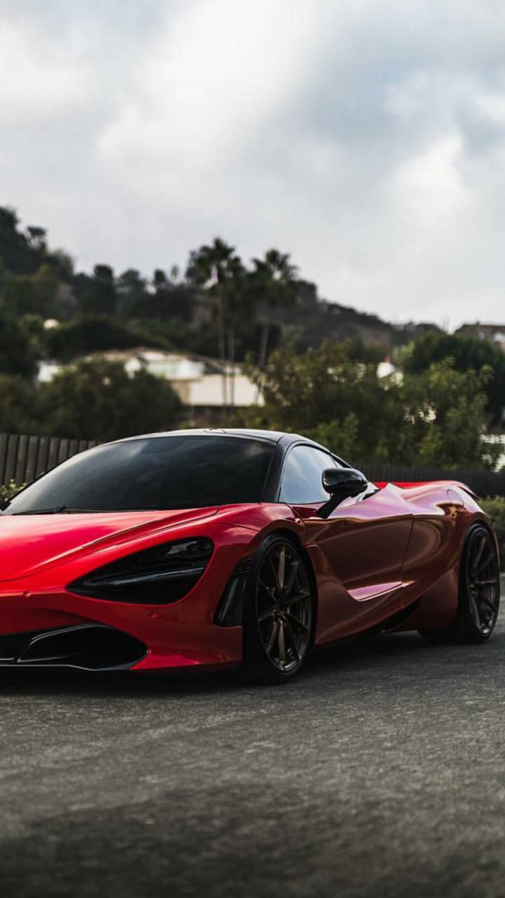 紅色McLaren 720S跑車停在瀝青路上，靠近棕櫚樹和山丘，天空多雲。