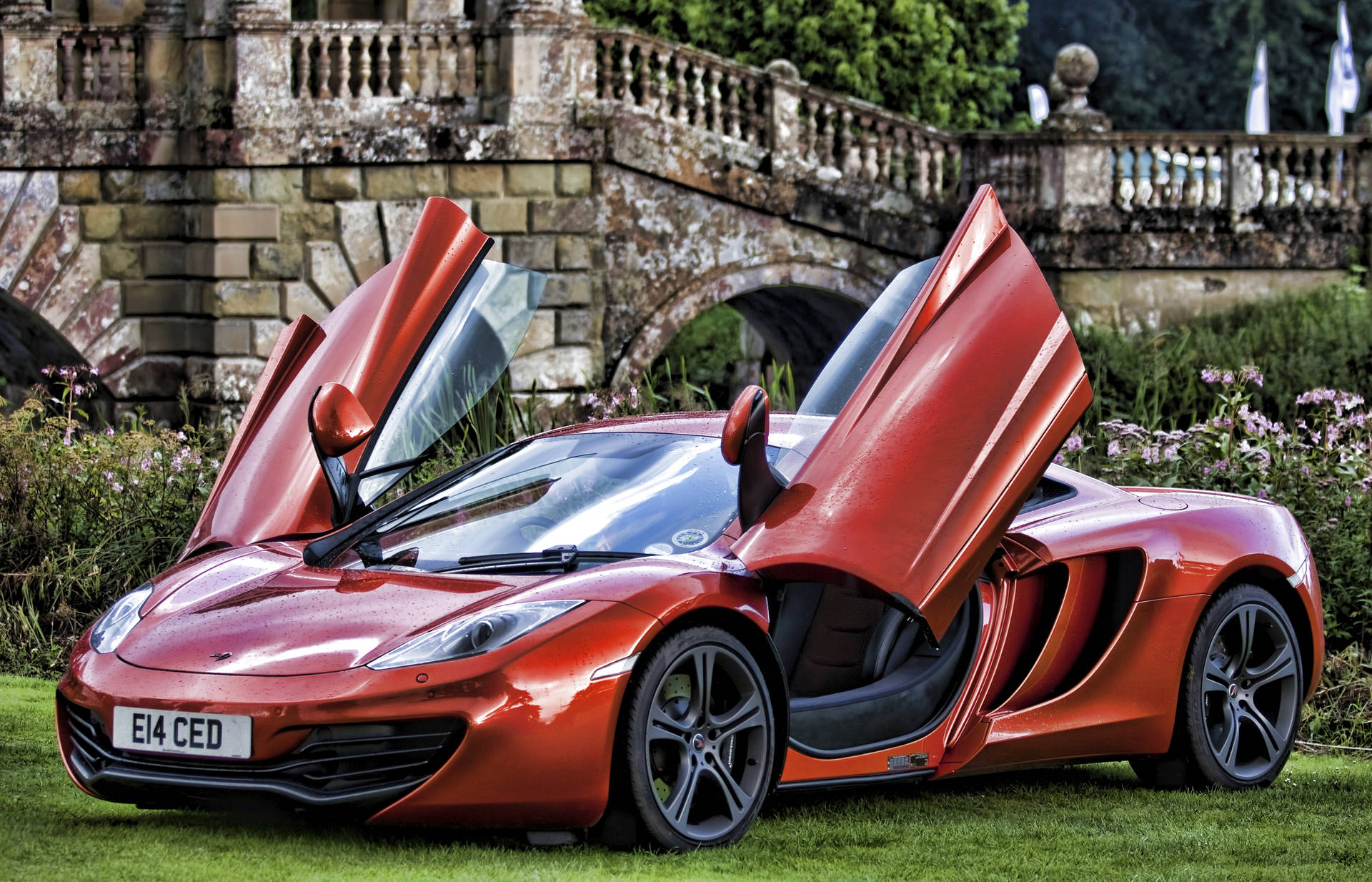 紅色McLaren，車門打開，停在石橋附近的草地上。