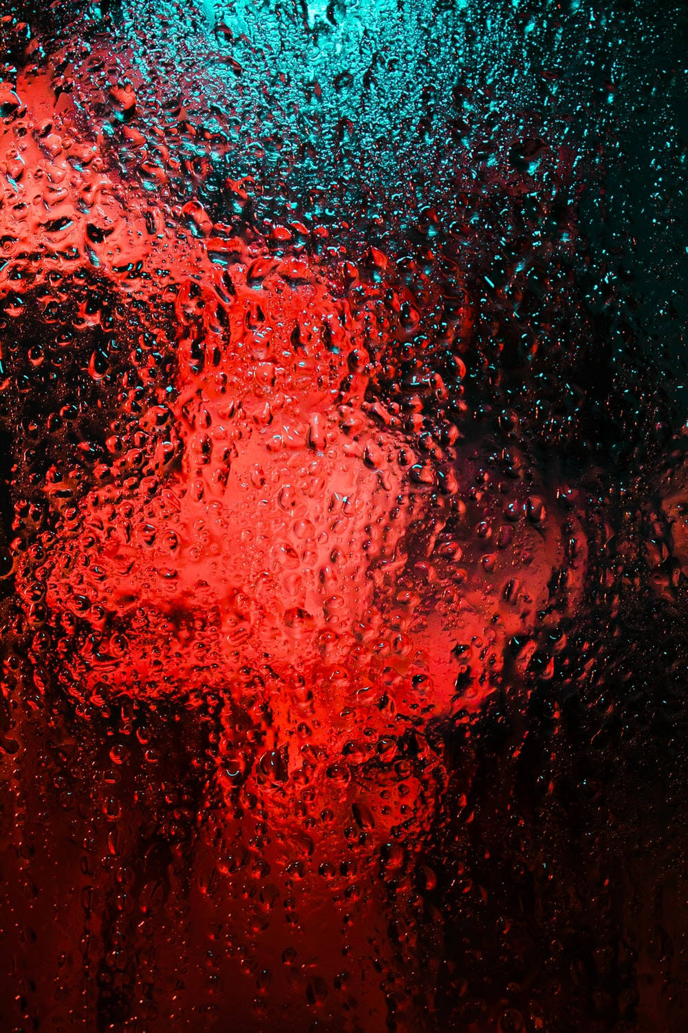 玻璃上的雨滴，紅色和藍綠色的燈光透射進來。