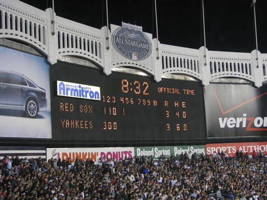 紅襪隊對洋基隊MLB比分 壁紙 — 夜晚擠滿人的棒球場，巨型記分板顯示洋基隊對紅襪隊的比分和Armitron汽車廣告。