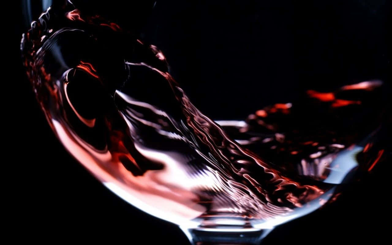 Red Wine Glass 桌布 壁紙 — 紅酒在杯中旋轉的特寫，背景為黑色，光線效果強烈。