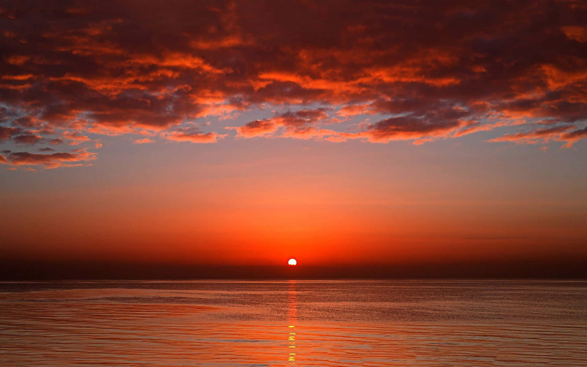 紅霞暮色下的海洋 壁紙 — 熾熱的夕陽將天空和寧靜的水面染成鮮豔的橙色和紅色色調，太陽沉入地平線以下。