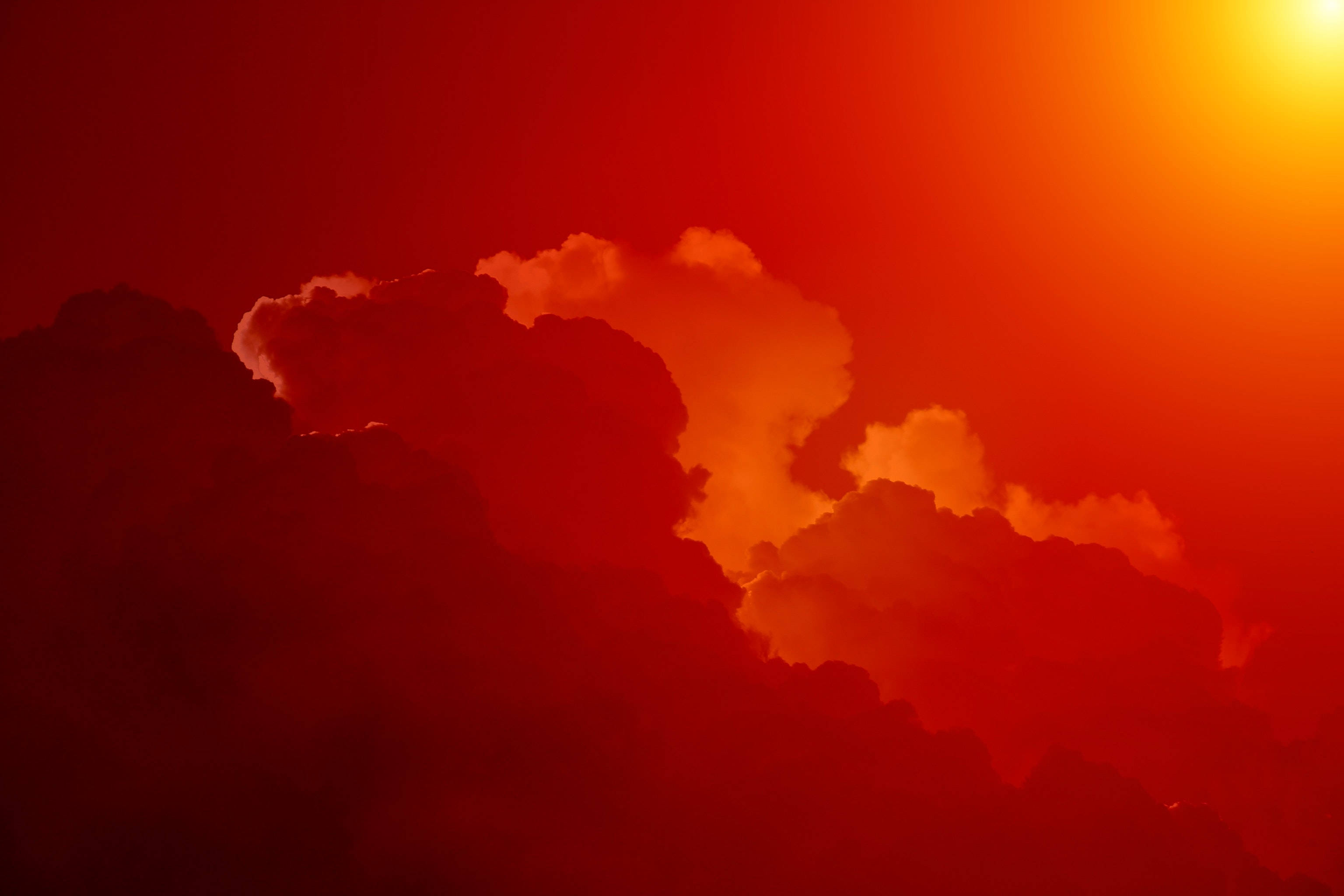 紅霞雲影的唯美天空 壁紙 — 戲劇性的雲層散發出火橙色和深紅色的光芒，一輪明亮的太陽從右上角穿透而出。