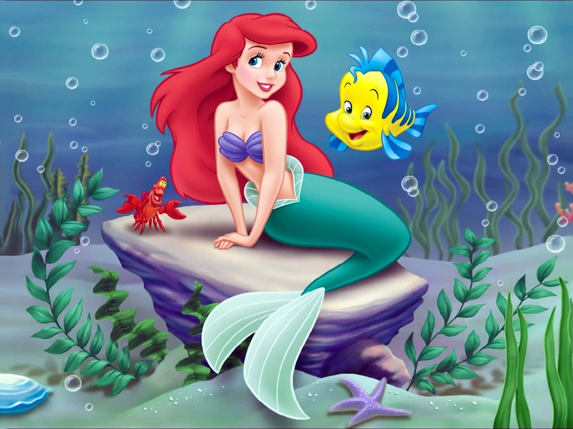 The Little Mermaid 桌布 壁紙 — 紅髮美人魚艾莉爾坐在岩石上微笑，旁邊是她的黃色魚朋友和紅色螃蟹，在陽光照射的水下場景中。