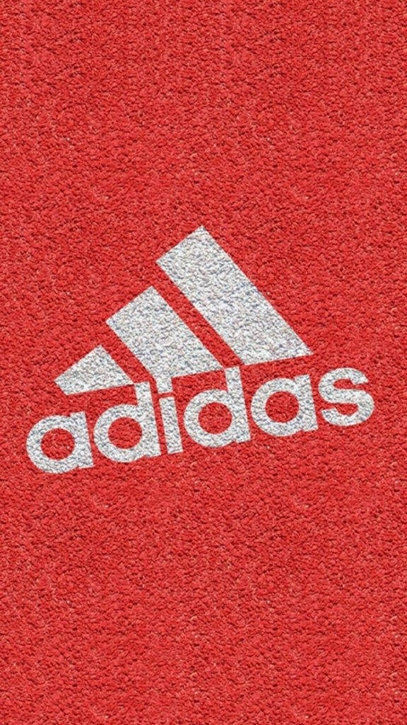 紋理地板與阿迪達斯 iPhone 標誌 壁紙 — 白色Adidas標誌在紋理紅色運動地板上的特寫。