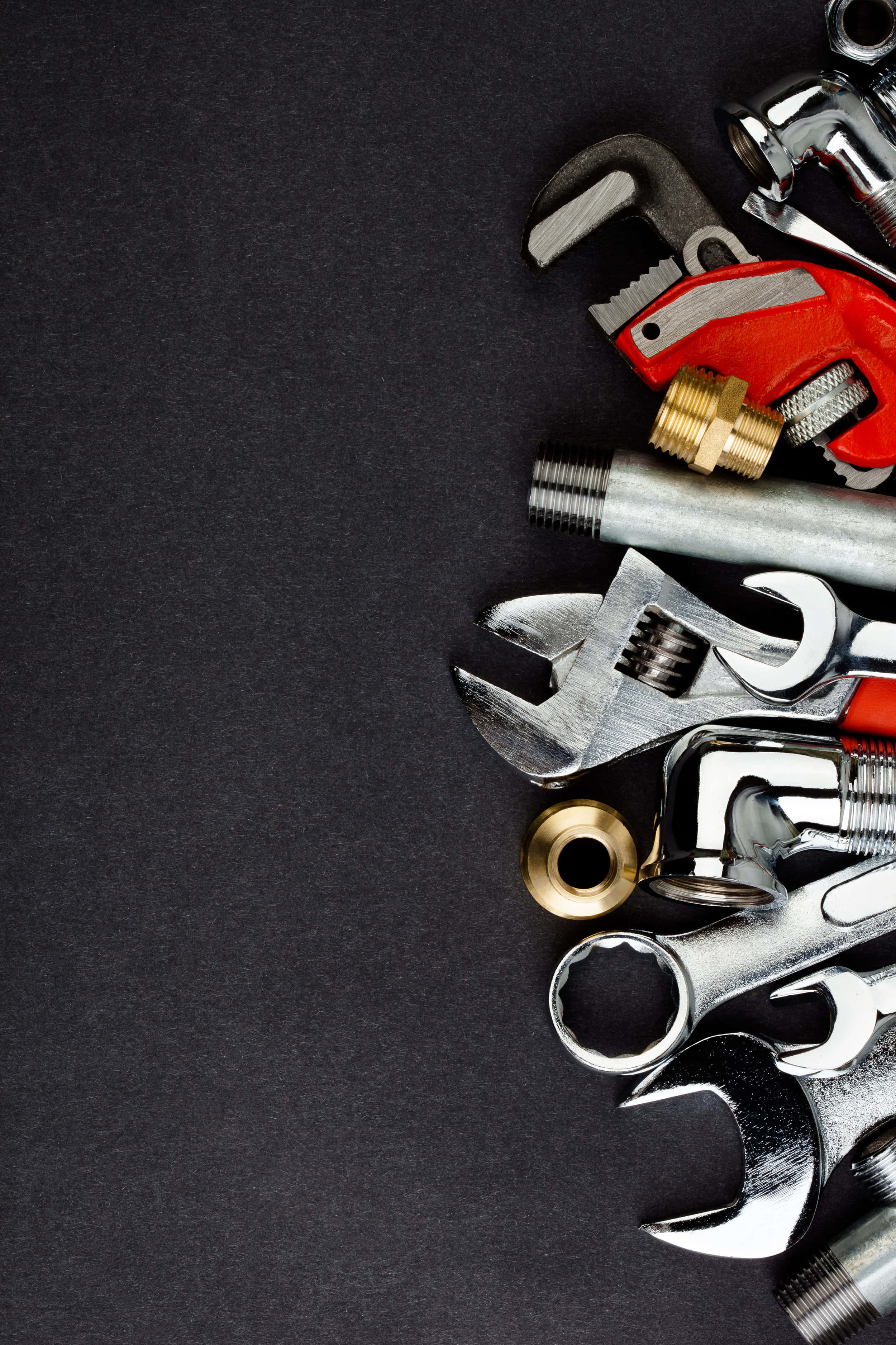 紋理黑色背景上的 plumbing 工具 壁紙 — 一系列閃亮的鍍鉻和紅色手柄的水管工具，對角排列在深色紋理表面上。