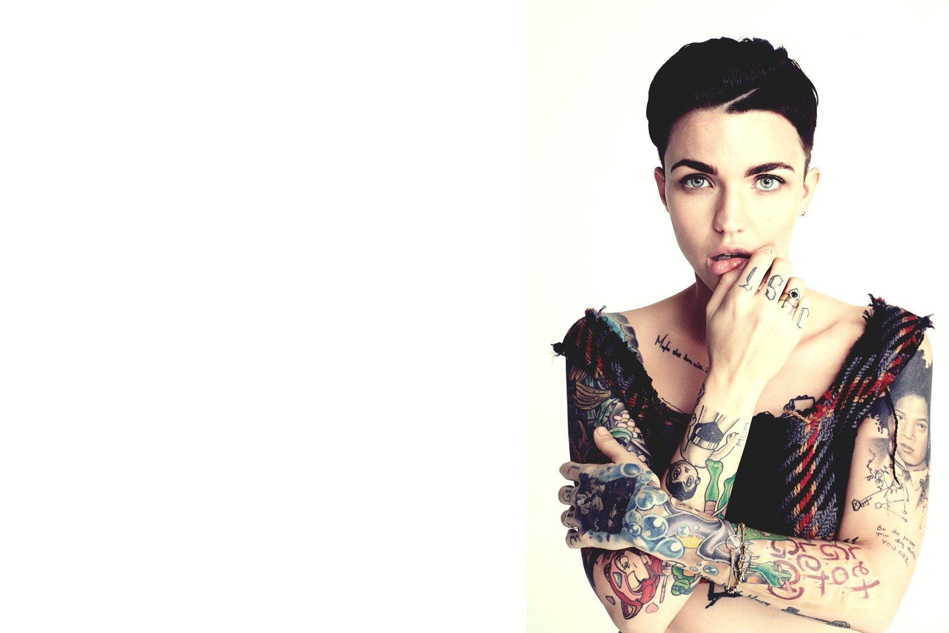 紋身 Ruby Rose 壁紙 — 一位短黑髮、擁有眾多彩色紋身的女性，用帶有紋身的手觸摸嘴唇，凝視著。